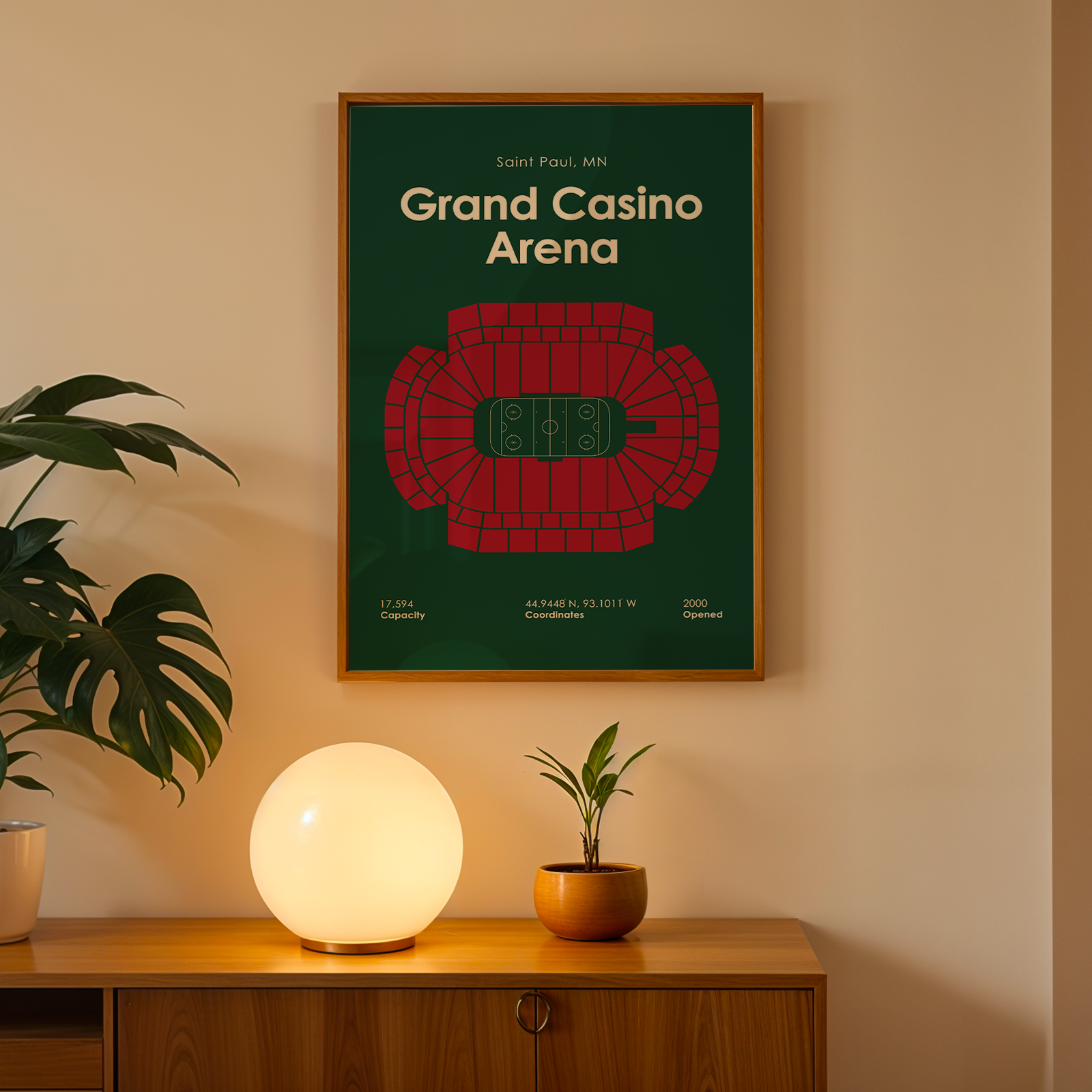Poster of Grand Casino Arena on a wall above a wooden cabinet with a lamp and plant.