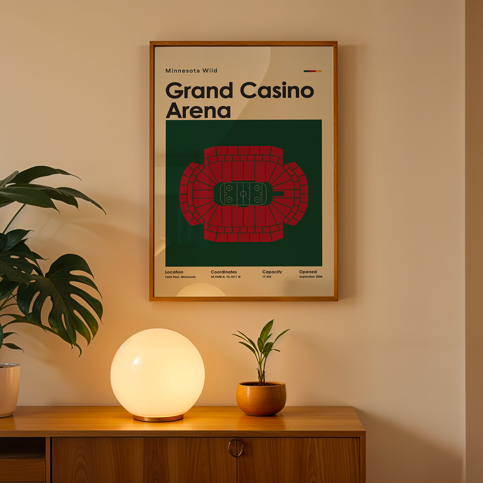 Framed poster of Grand Casino Arena on a wall with a plant and lamp on a wooden surface below.