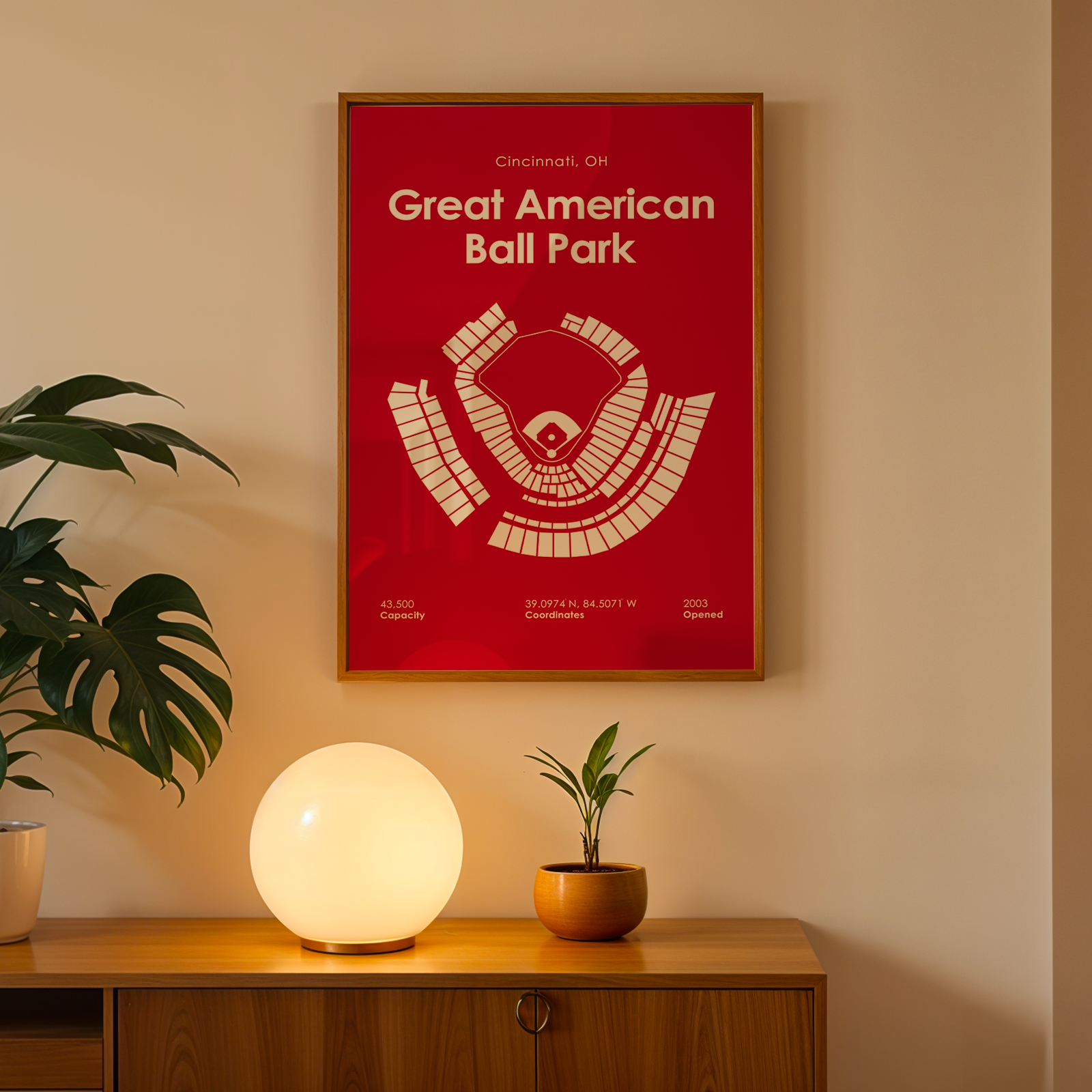 Framed poster of Great American Ball Park on a wall with a plant and lamp below.