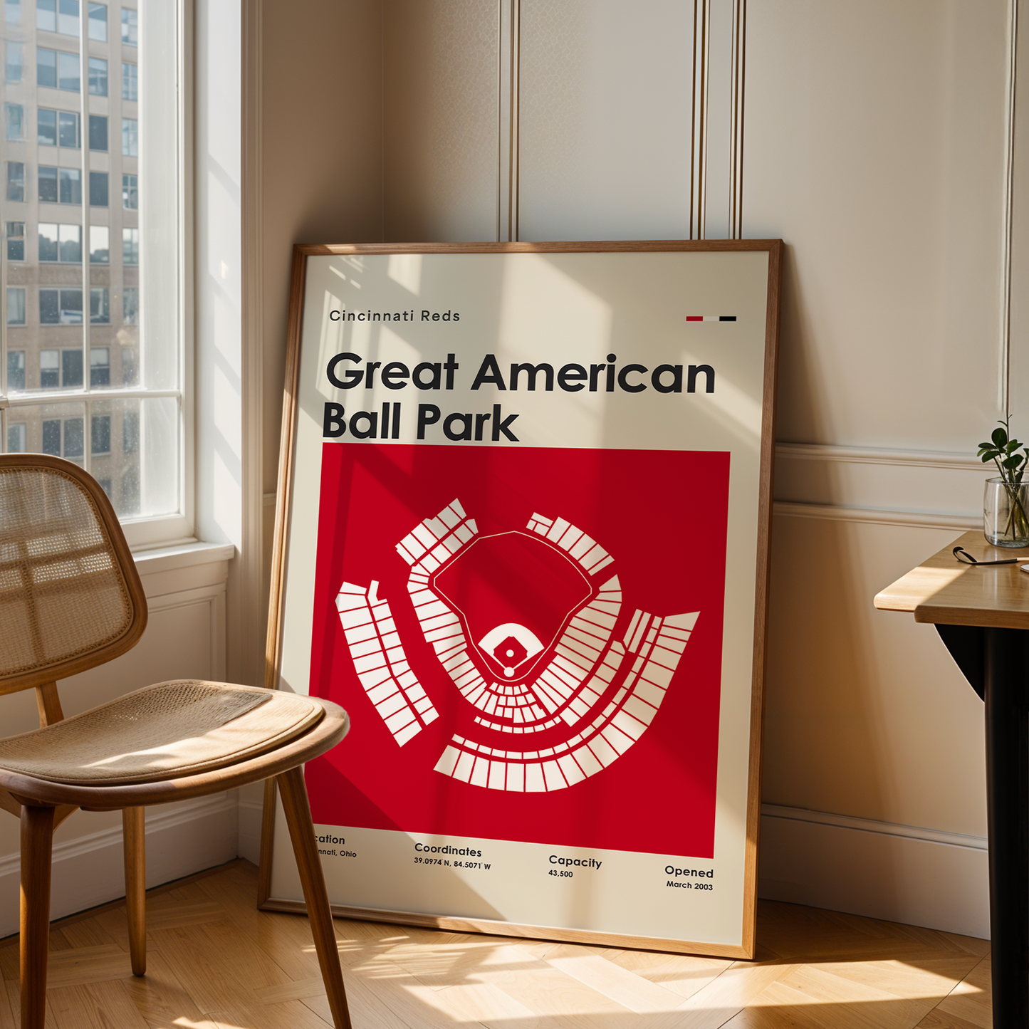 Framed poster of Great American Ball Park in a room with a chair and table.