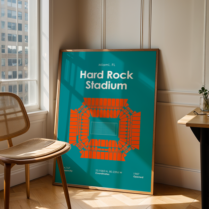 Framed poster of Hard Rock Stadium in Miami, FL, leaning against a wall in a room with a chair and table.