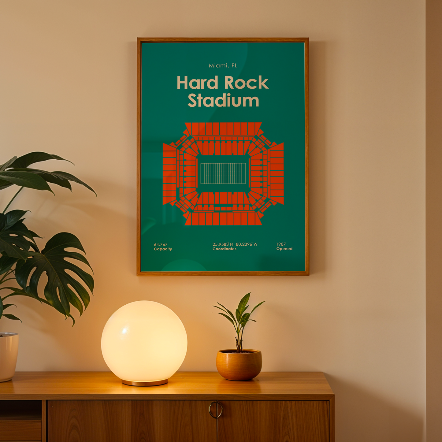 Framed poster of Hard Rock Stadium on a wall above a wooden cabinet with decorative items.