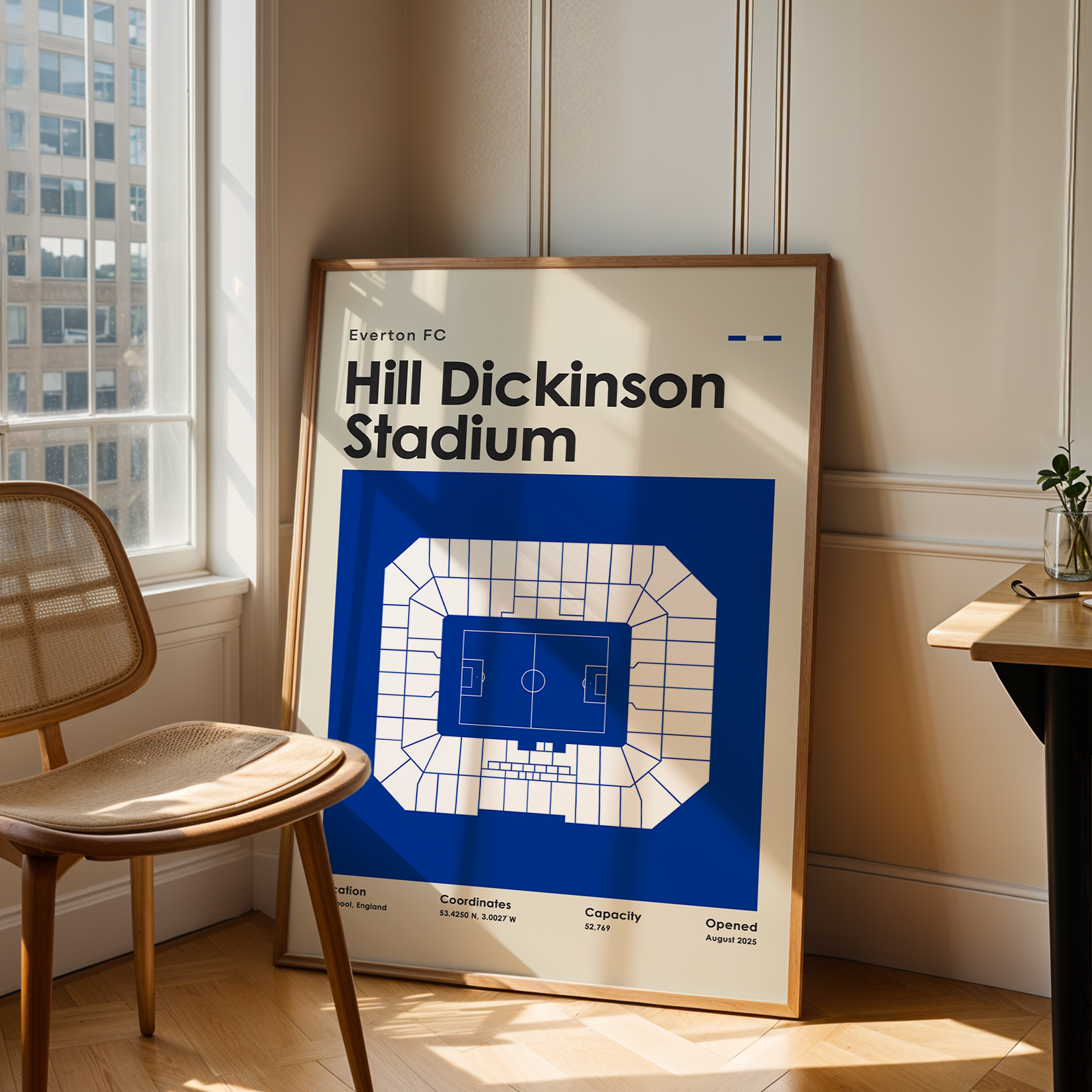 Framed poster of Hill Dickinson Stadium in a room with a chair and table.