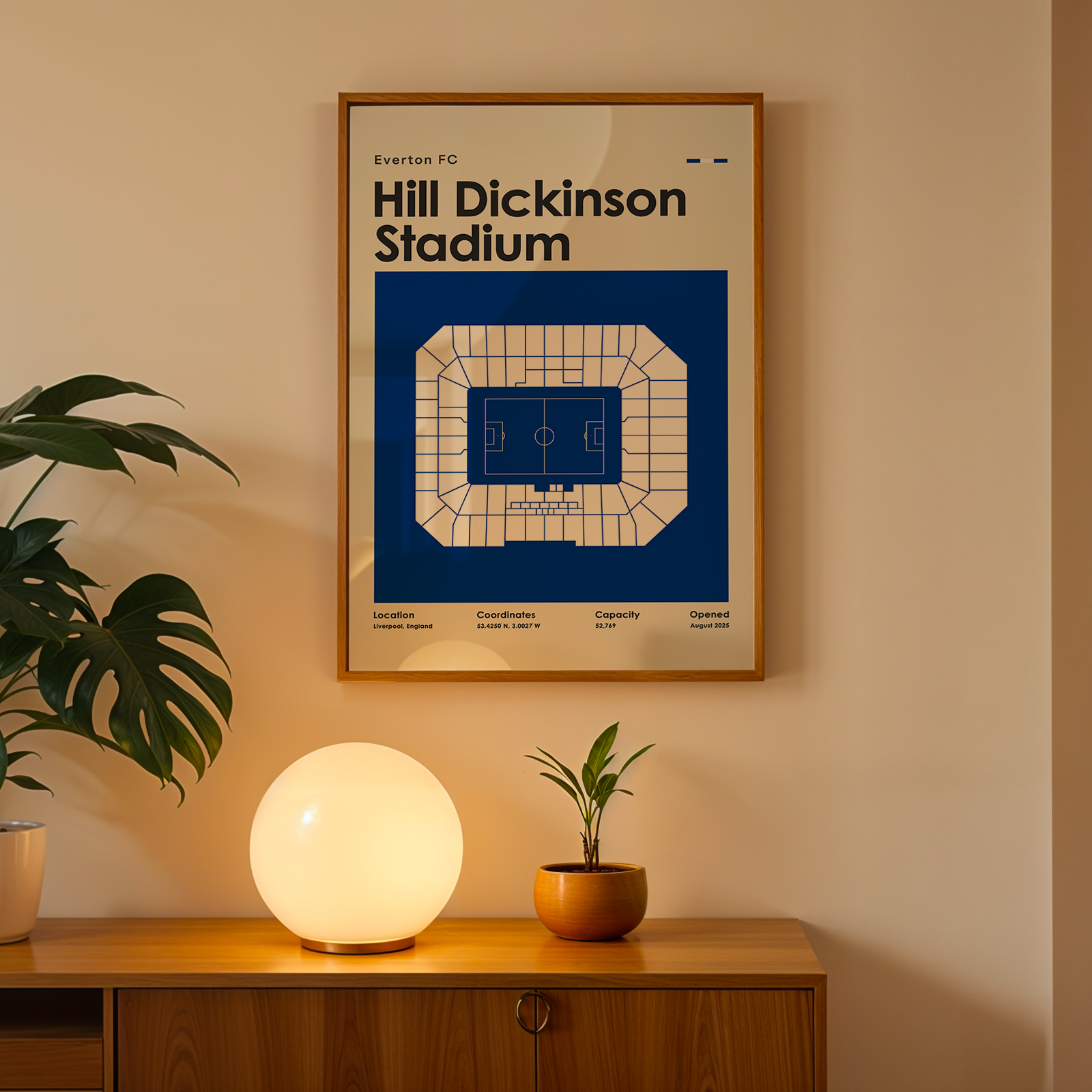 Framed poster of Hill Dickinson Stadium on a wall above a wooden cabinet with decorative items.