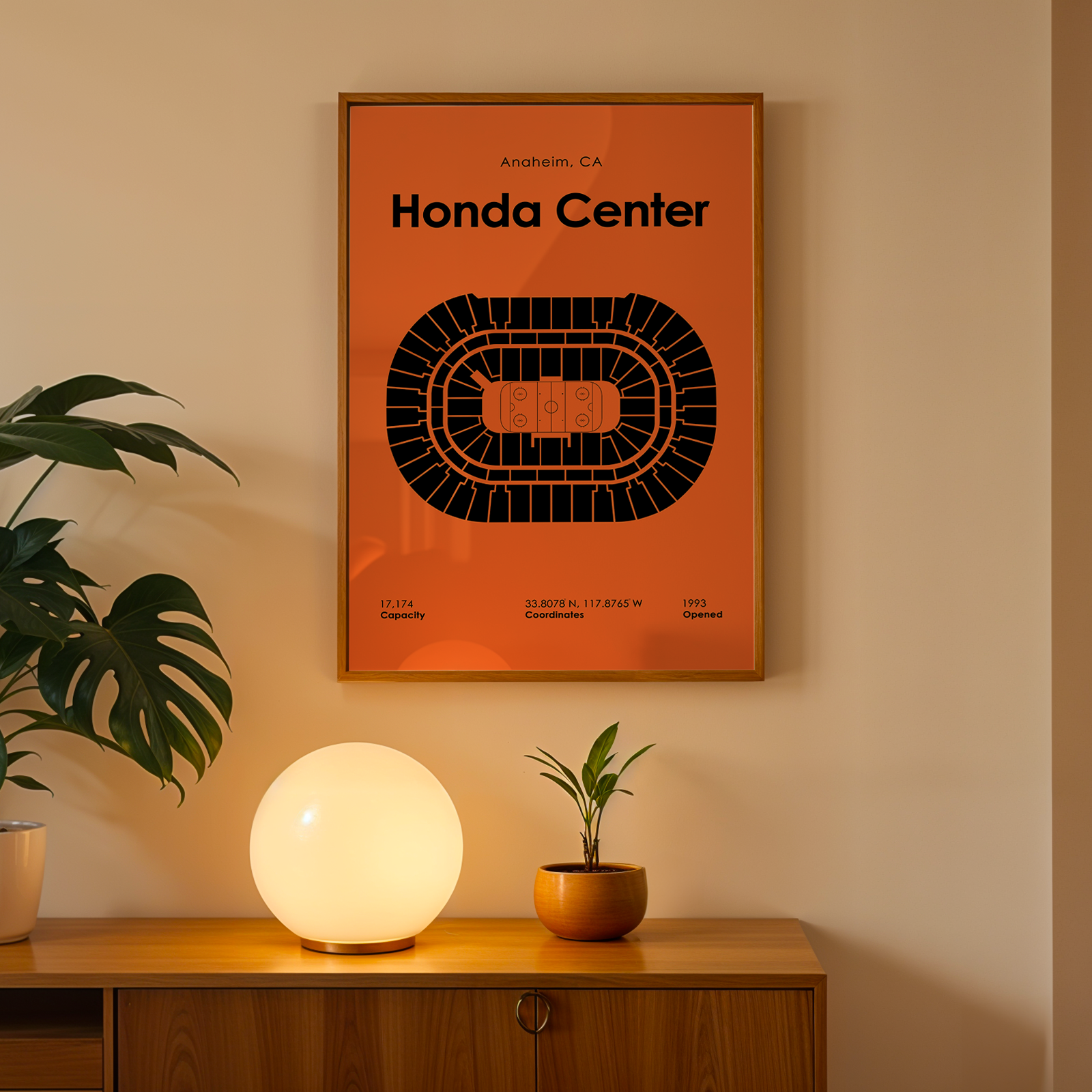Poster of Honda Center on a wall above a wooden cabinet with a lamp and plant.