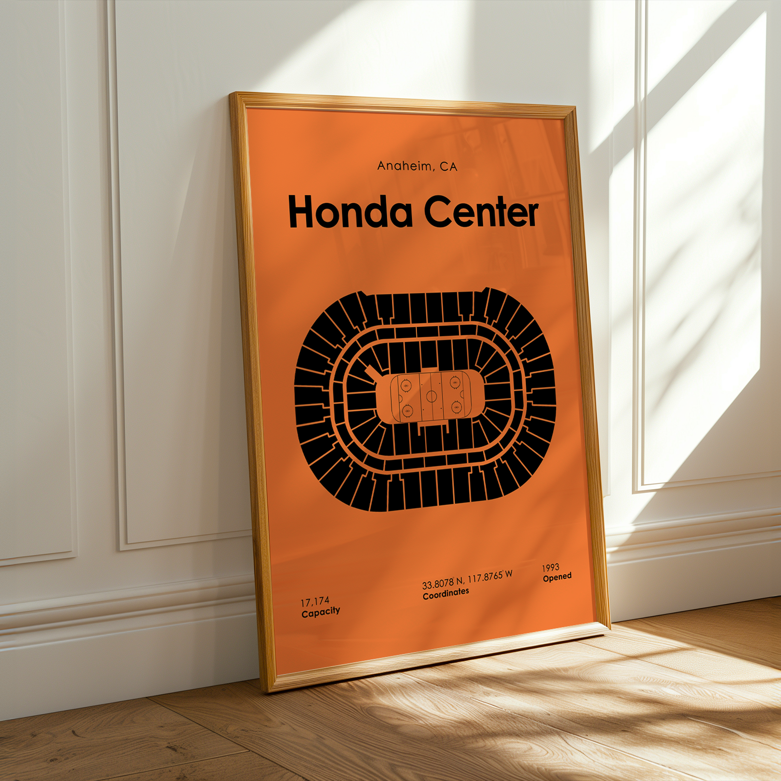 Framed poster of Honda Center layout on an orange background, leaning against a white wall.