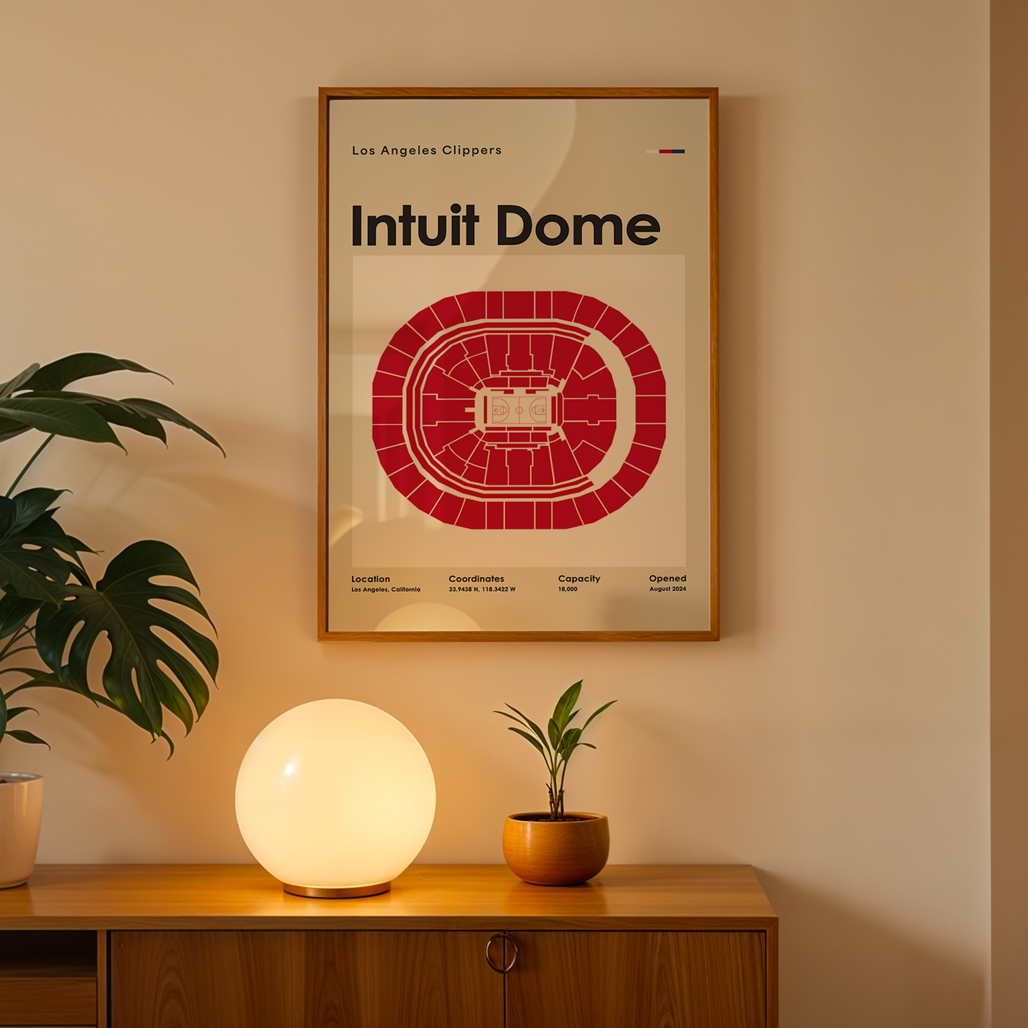 Framed poster of Intuit Dome on a wall above a wooden cabinet with decorative items.