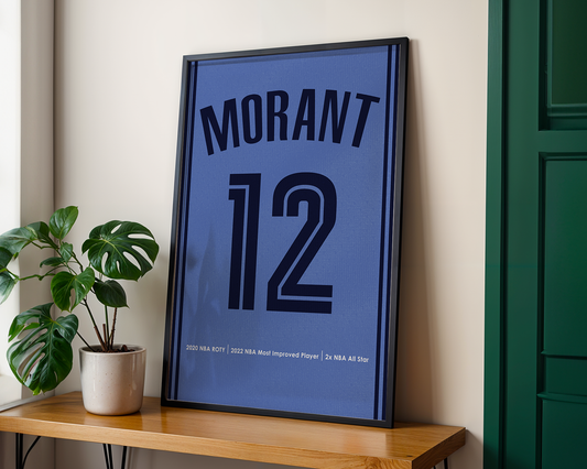 Framed sports jersey with 'Morant 12' on a wooden shelf next to a plant.