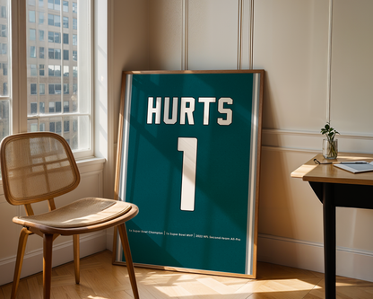 Framed poster with 'HURTS' and number '1' in a room with a chair and table.