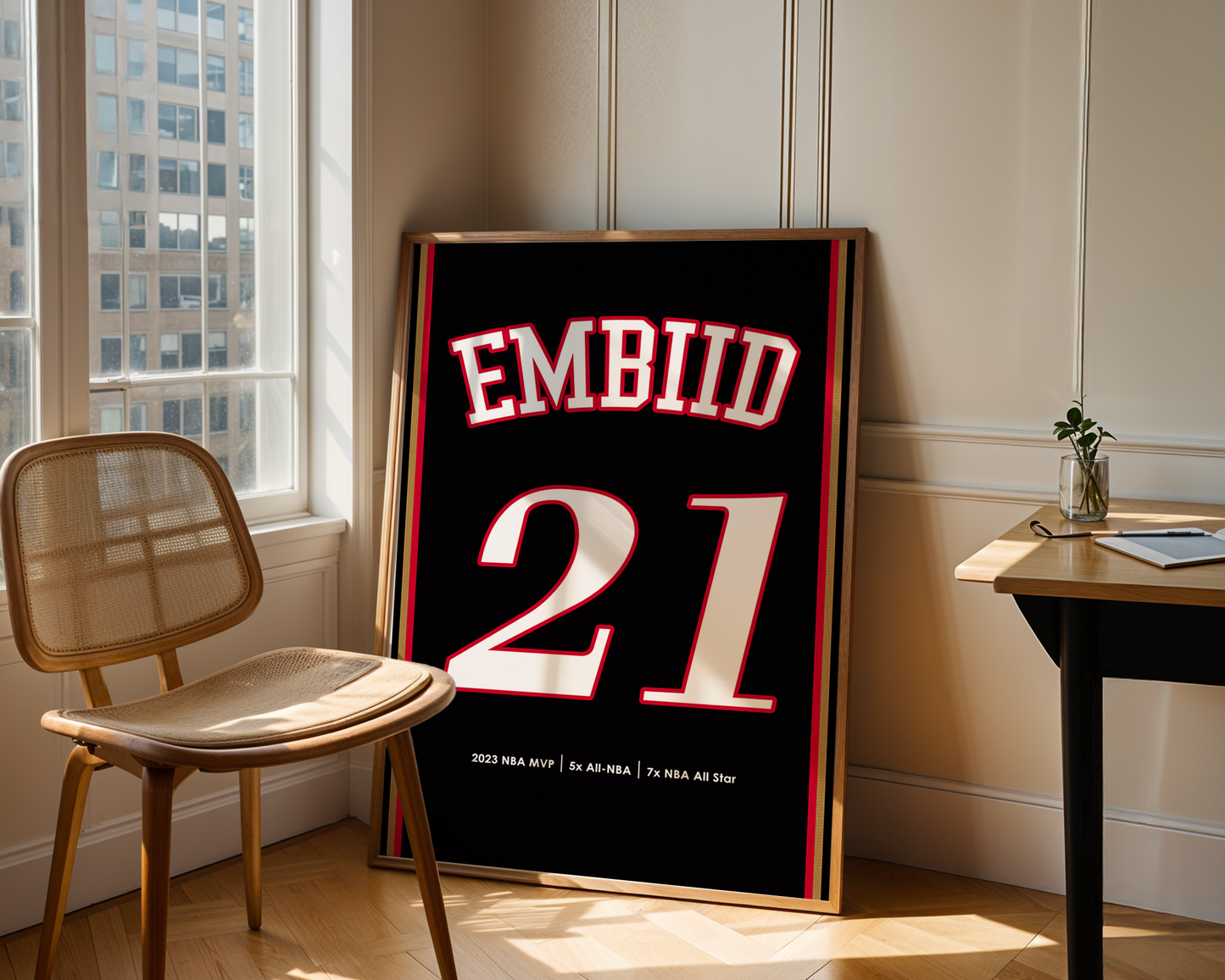 Framed sports jersey with 'EMBIID 21' in a room with a chair and table.