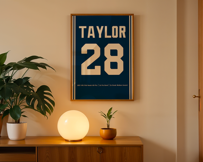 Framed poster with 'Taylor 28' on a wall above a wooden cabinet with decorative items.