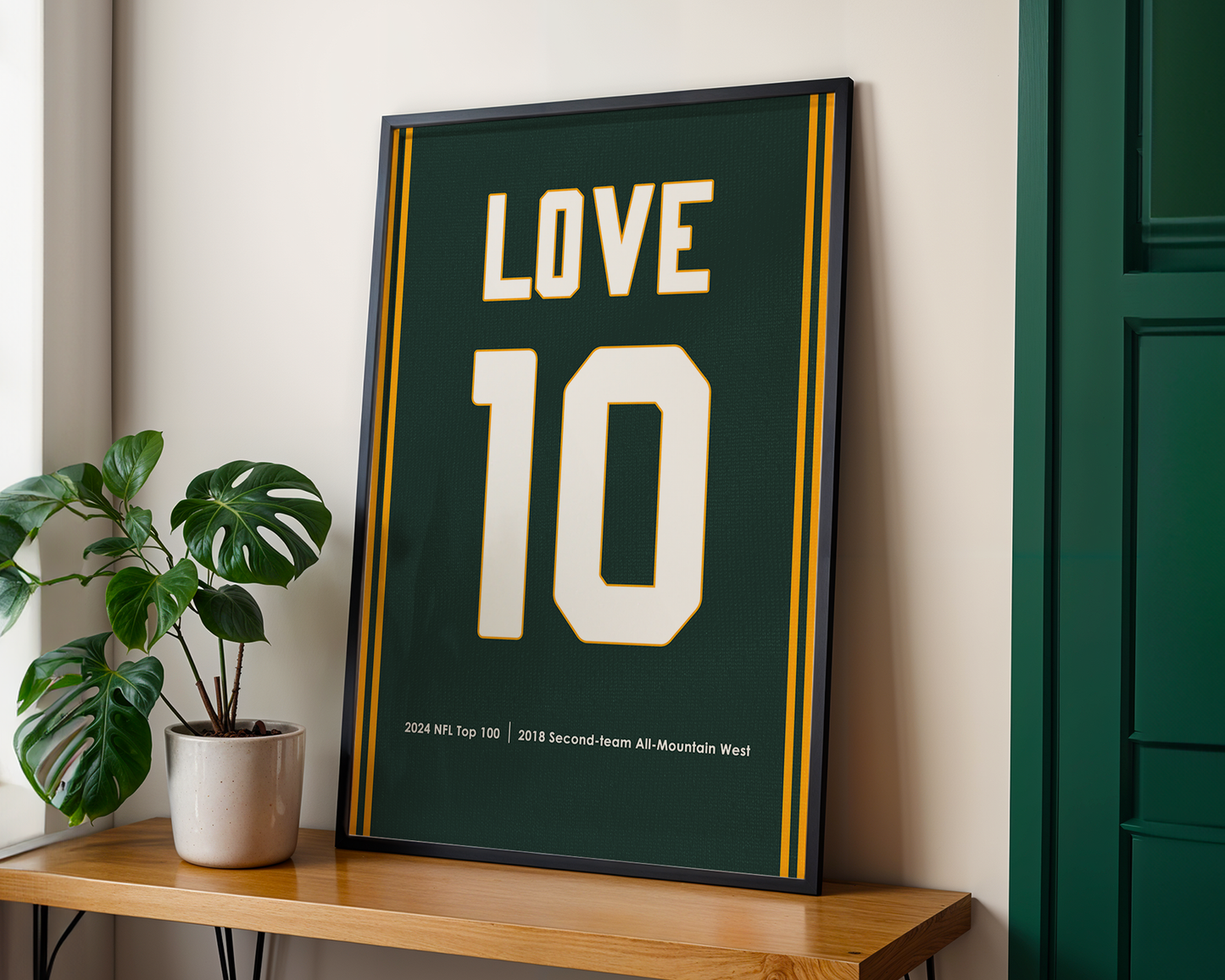 Framed poster with 'LOVE 10' on a wooden shelf next to a plant