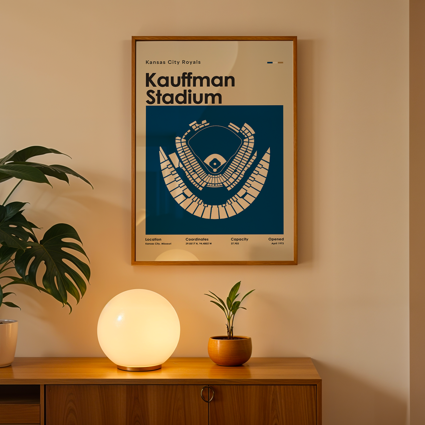 Framed poster of Kauffman Stadium on a wall above a wooden cabinet with decorative items.