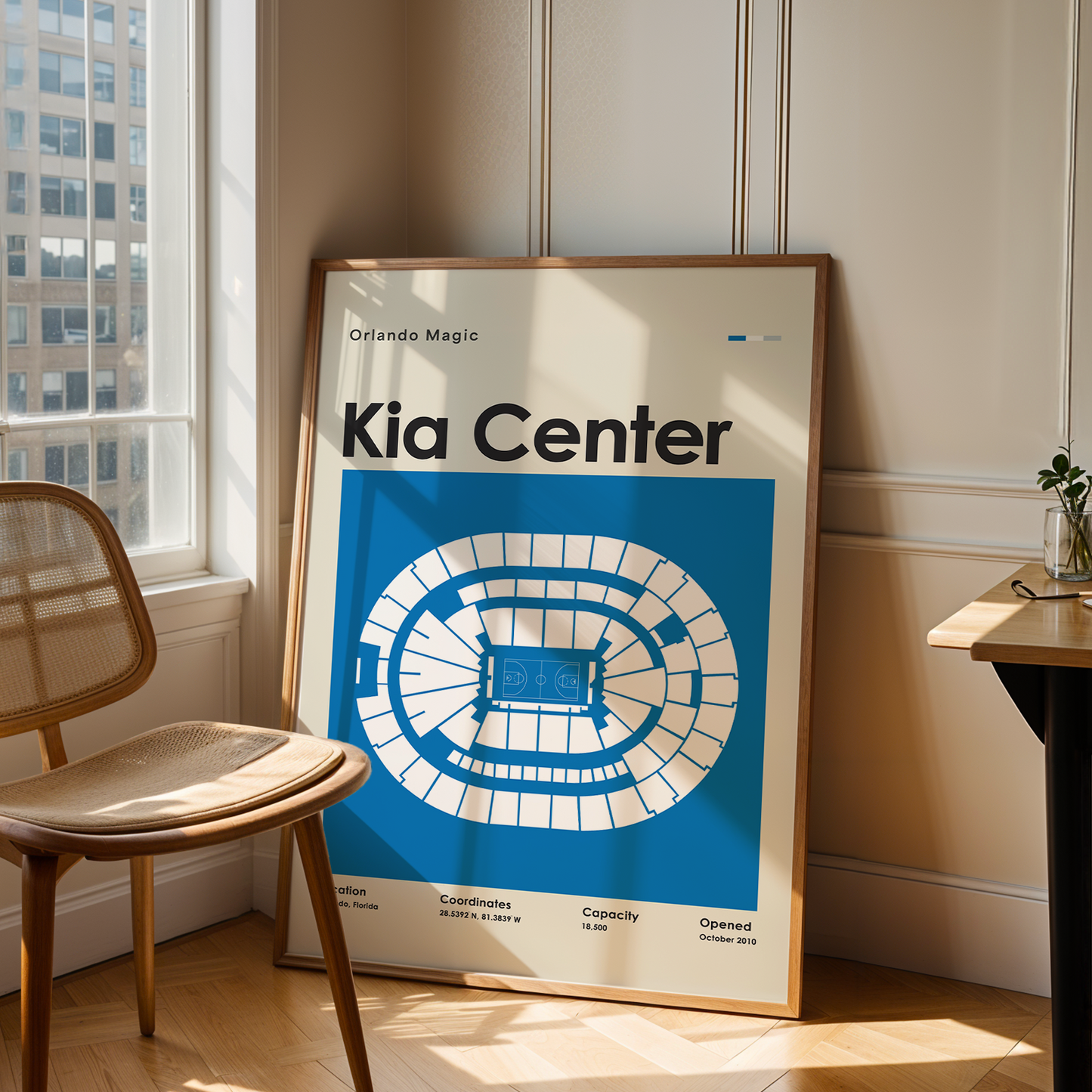 Framed poster of the Kia Center in a room with a chair and table.
