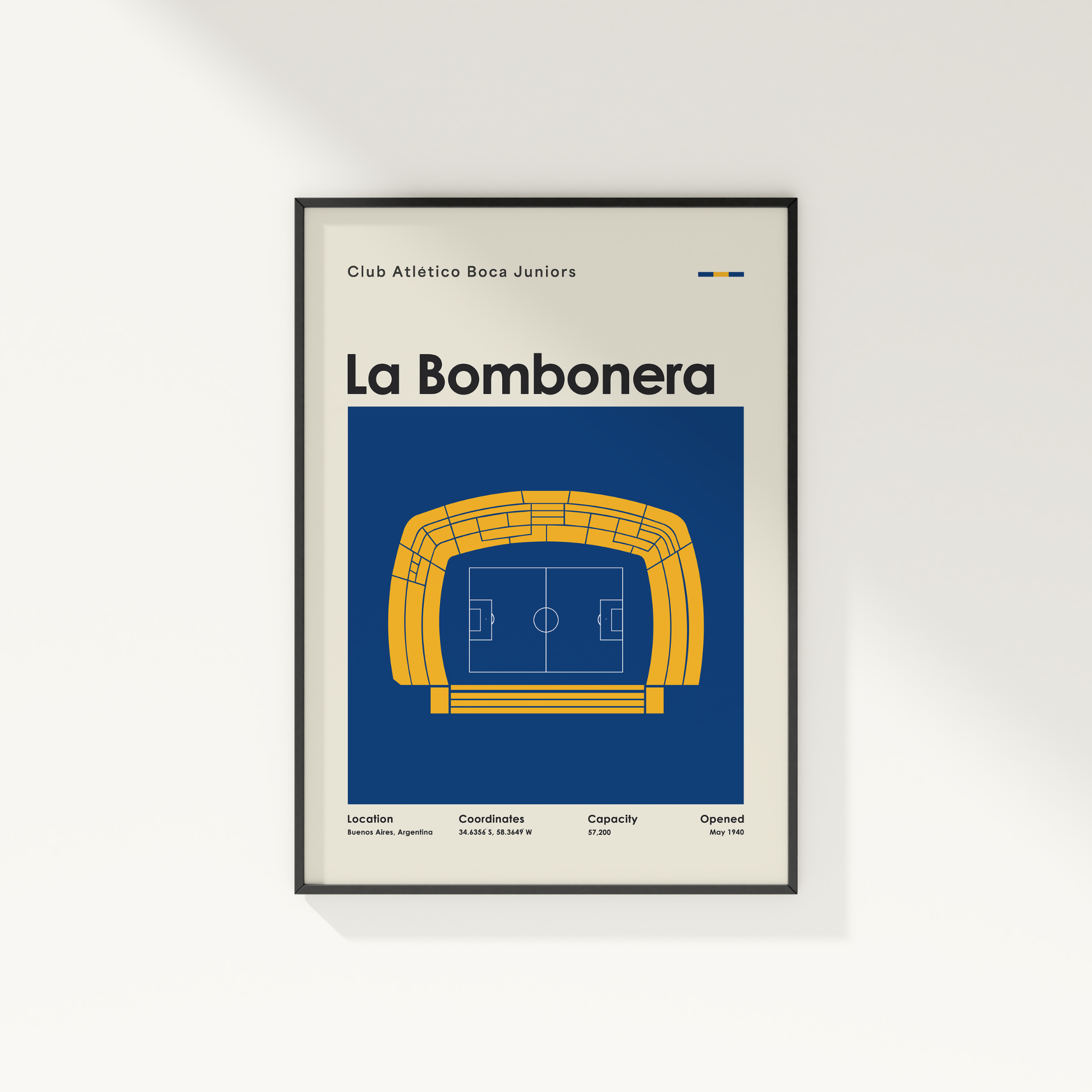 A framed poster print featuring a stylized football stadium illustration with the text 'La Bombonera' and 'Club Atletico Boca Juniors' on a light background, shown hanging on a white wall.