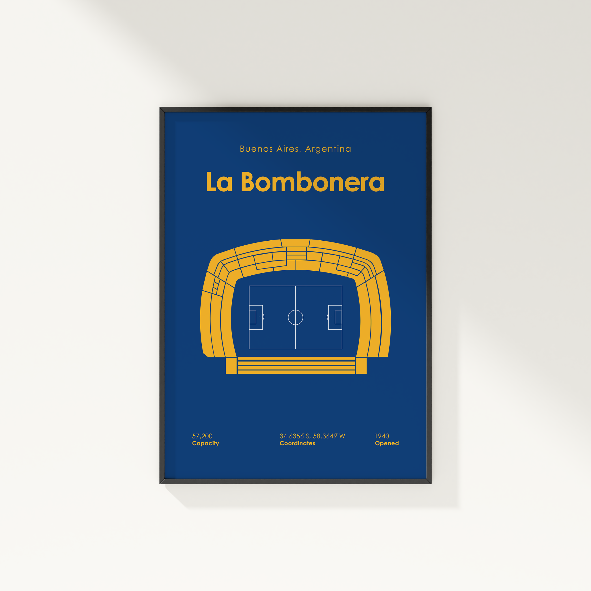 A framed sports poster of La Bombonera stadium in Buenos Aires, Argentina, featuring a yellow stadium diagram on a dark blue background, shown hanging on a light gray wall.