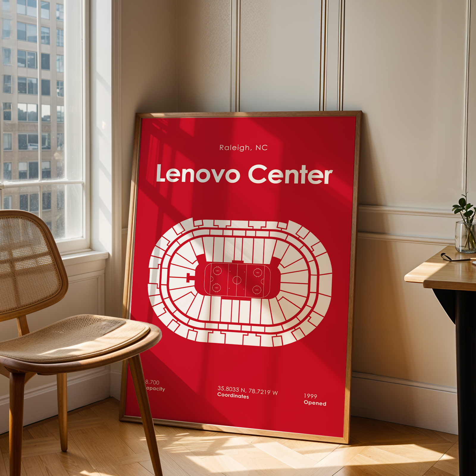 Framed poster of Lenovo Center in Raleigh, NC, leaning against a wall in a room with a chair and window.