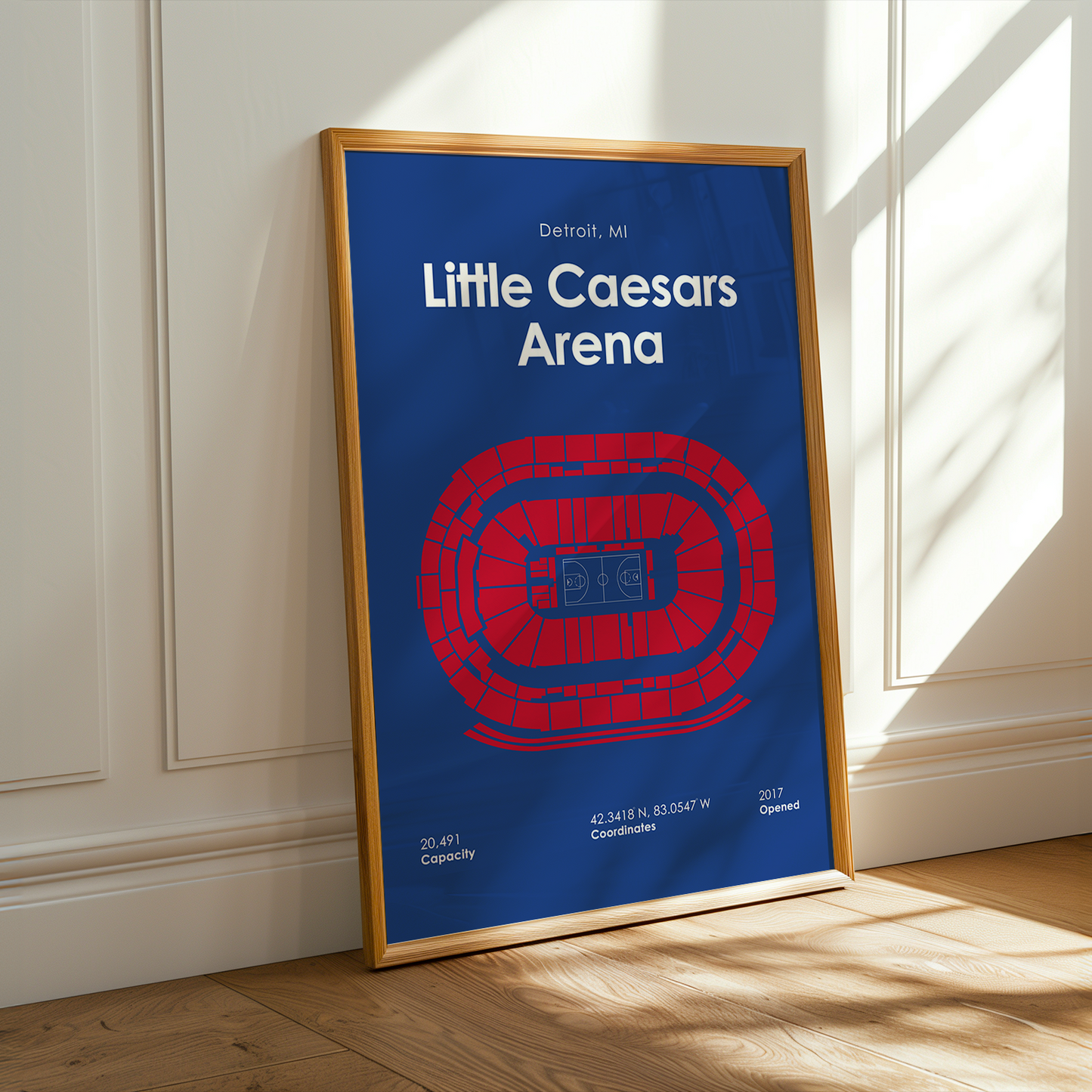 Framed poster of Little Caesars Arena on a wall with sunlight casting shadows.