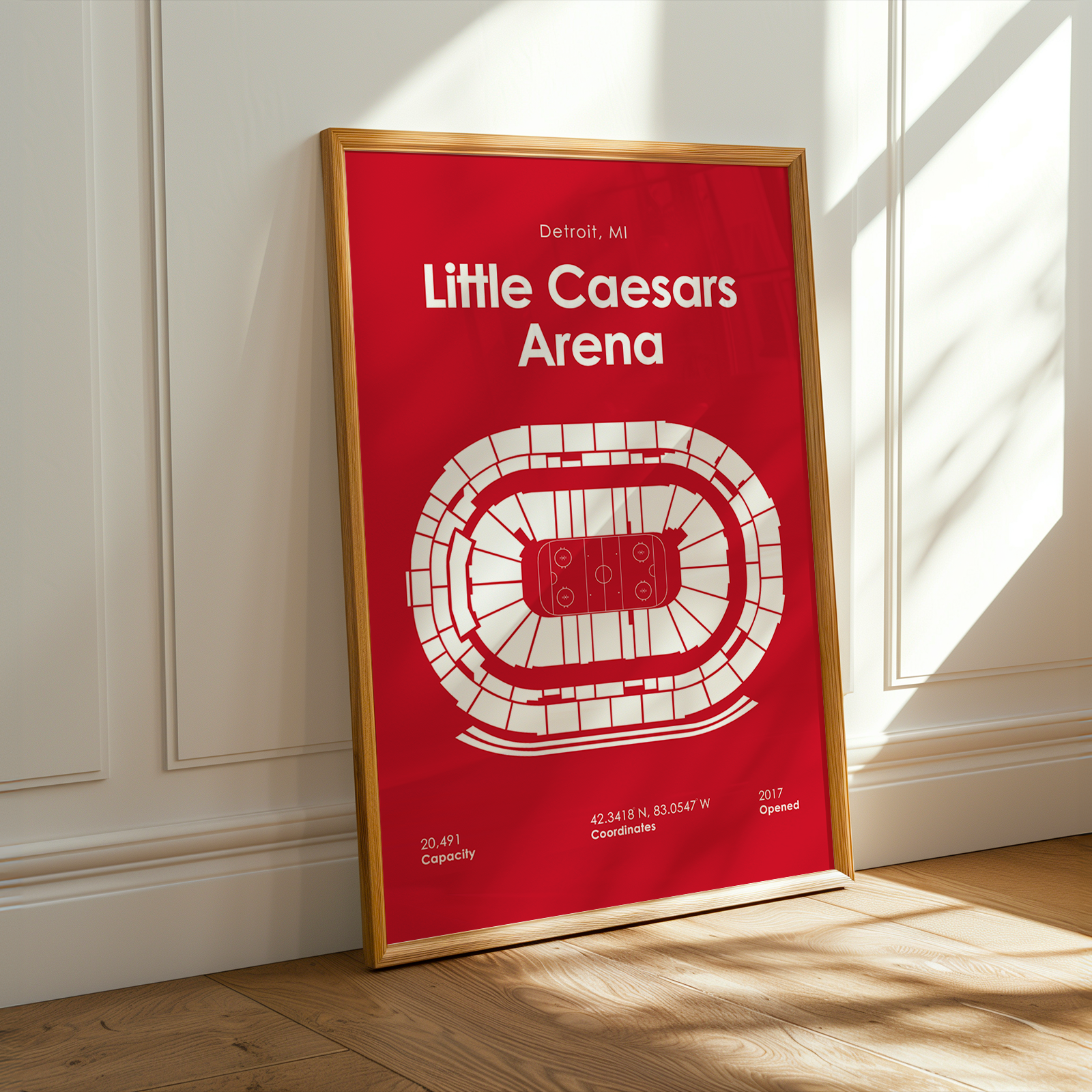 Framed poster of Little Caesars Arena on a wall with sunlight casting shadows.