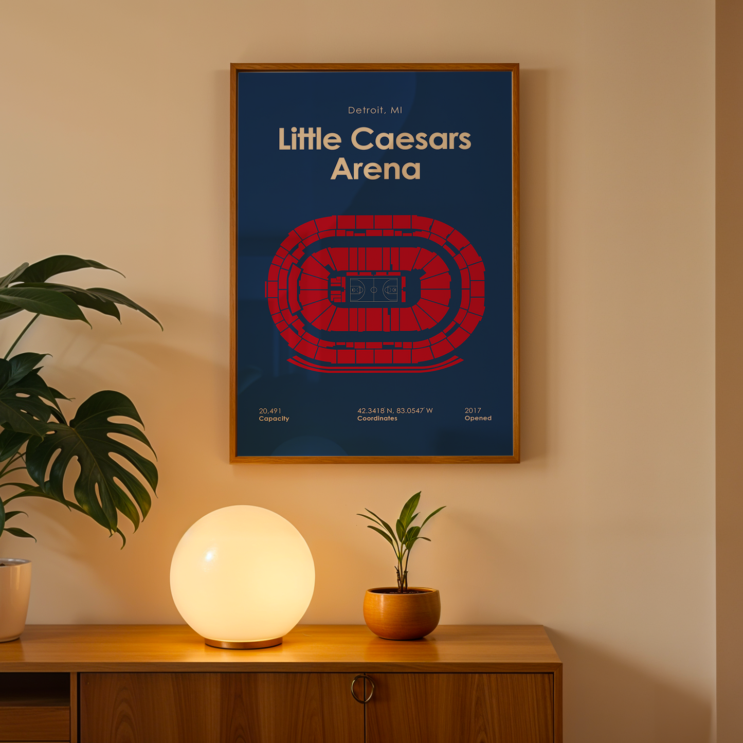 Framed poster of Little Caesars Arena on a wall above a wooden cabinet with decorative items.