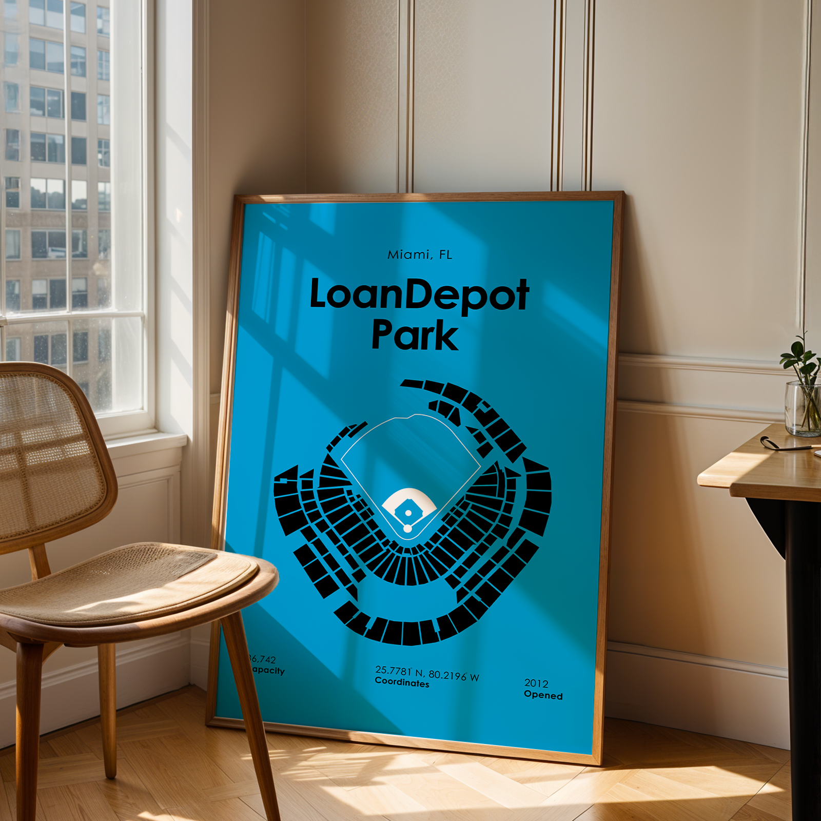 Framed poster of LoanDepot Park in Miami, FL leaning against a wall in a room with a chair and table.