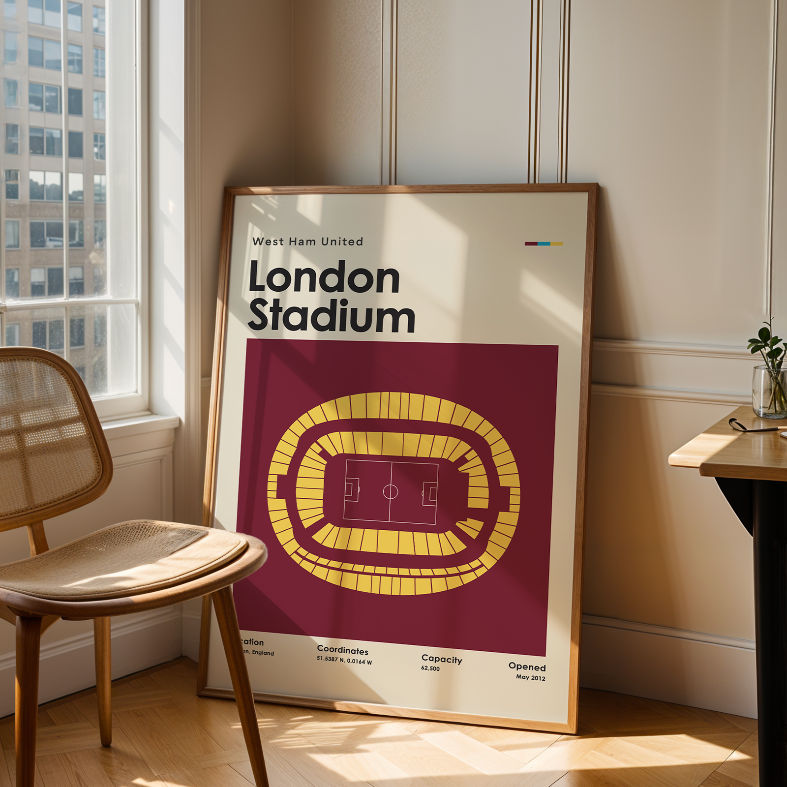 Framed poster of London Stadium in a room with a chair and table.