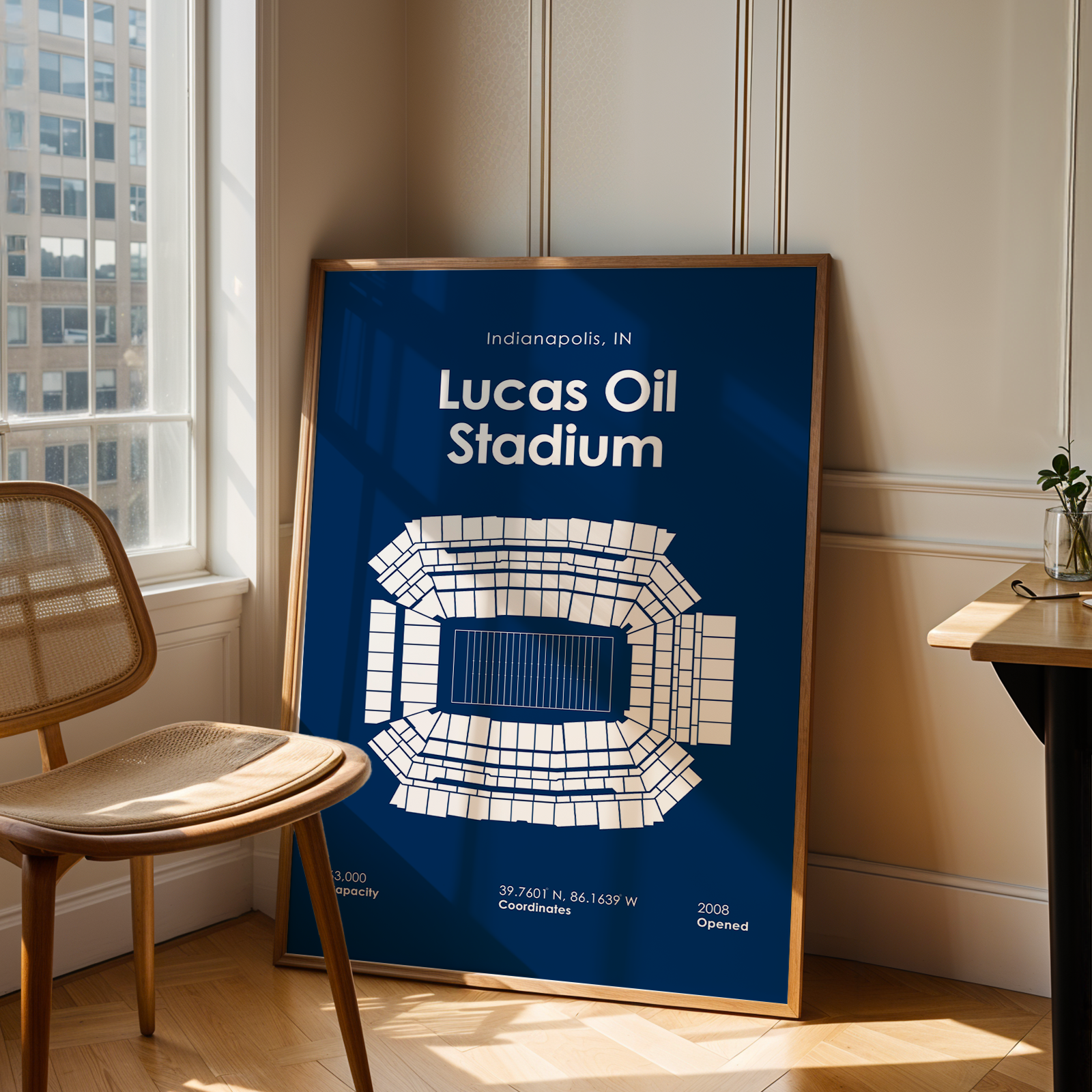 Framed poster of Lucas Oil Stadium in Indianapolis on a wall next to a chair and table.