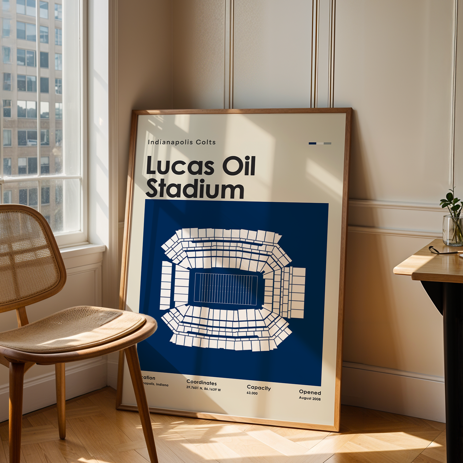Framed poster of Lucas Oil Stadium in a room with a chair and window.