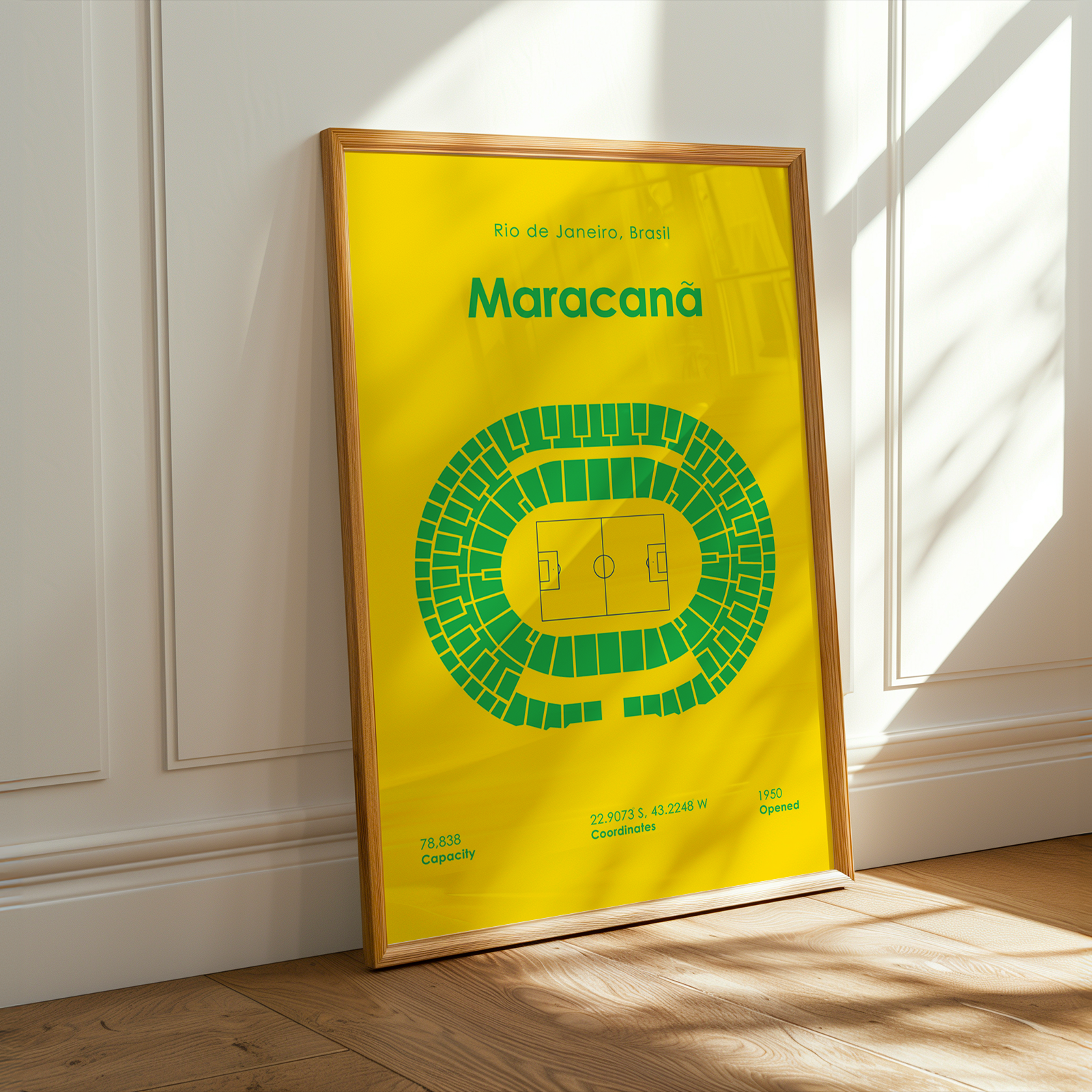 A framed yellow soccer stadium map poster of Maracana in Rio de Janeiro, leaning against a white paneled wall on a wooden floor with warm sunlight and window shadows.