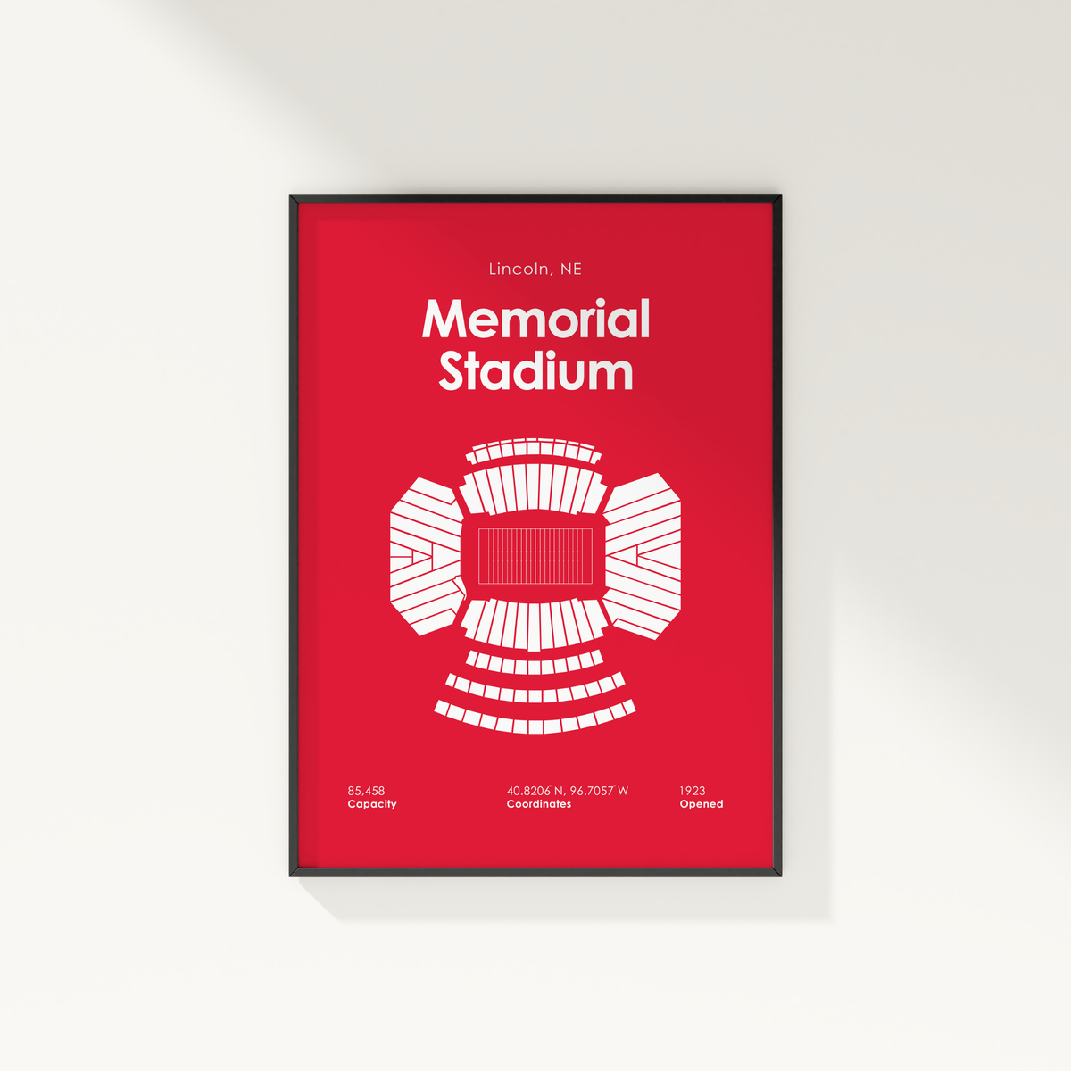 A framed minimalist poster of Memorial Stadium in Lincoln, Nebraska, featuring a bold red background and a white stadium floor plan diagram.