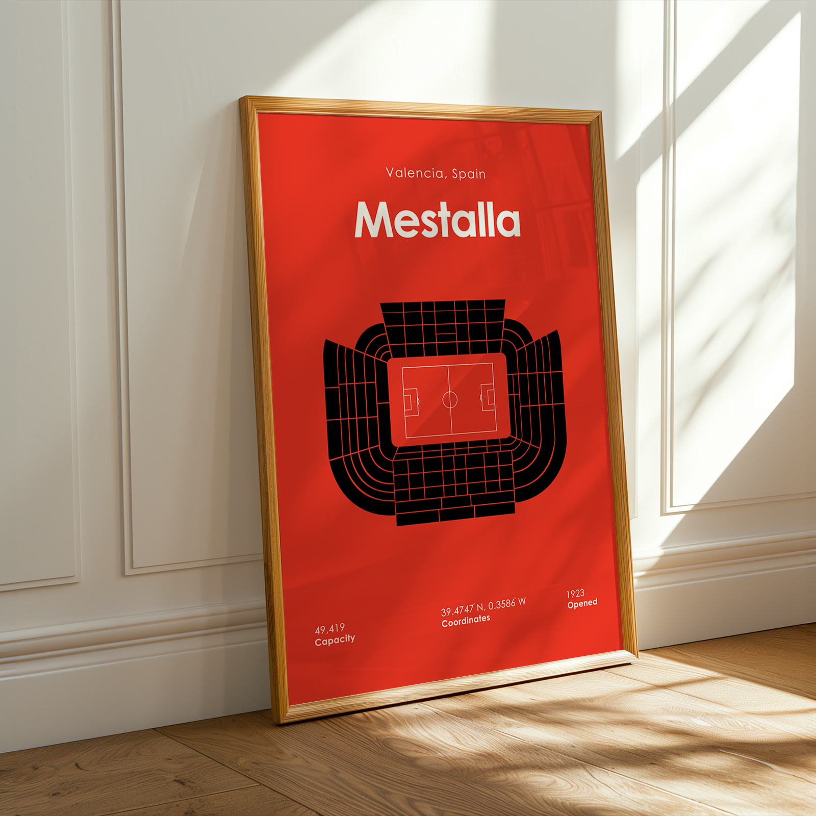 Framed poster of Mestalla stadium on a red background in a room with sunlight.