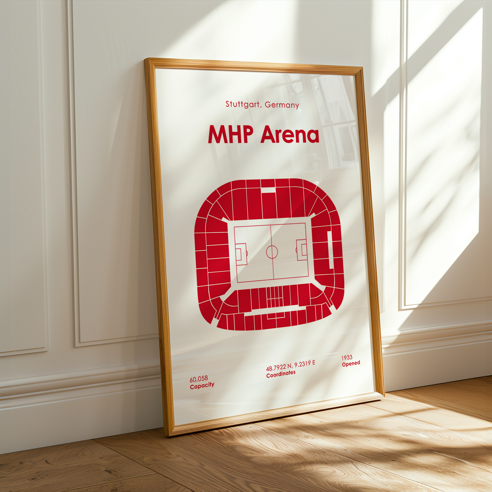 A framed minimalist stadium seating print for the MHP Arena in Stuttgart, Germany, leaning against a white paneled wall on a light wood floor with warm sunlight streaming in.