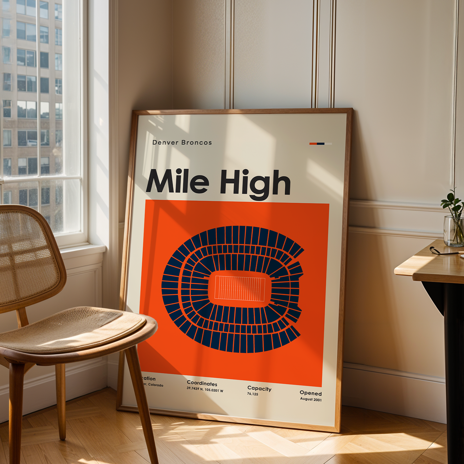 Framed 'Mile High' sports arena poster in a room with a chair and table.