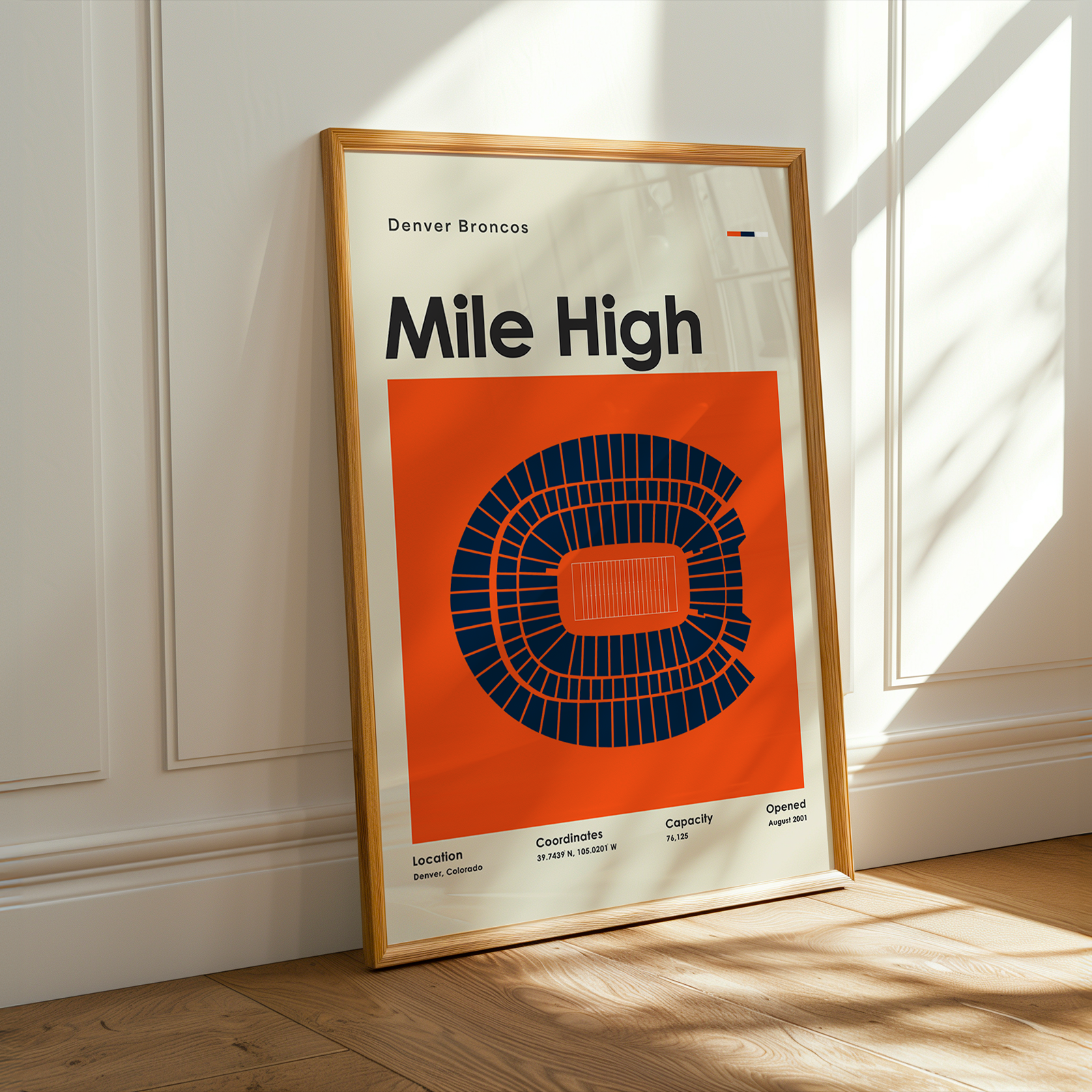 Framed poster of the Denver Broncos stadium layout on a wooden floor with sunlight streaming in.