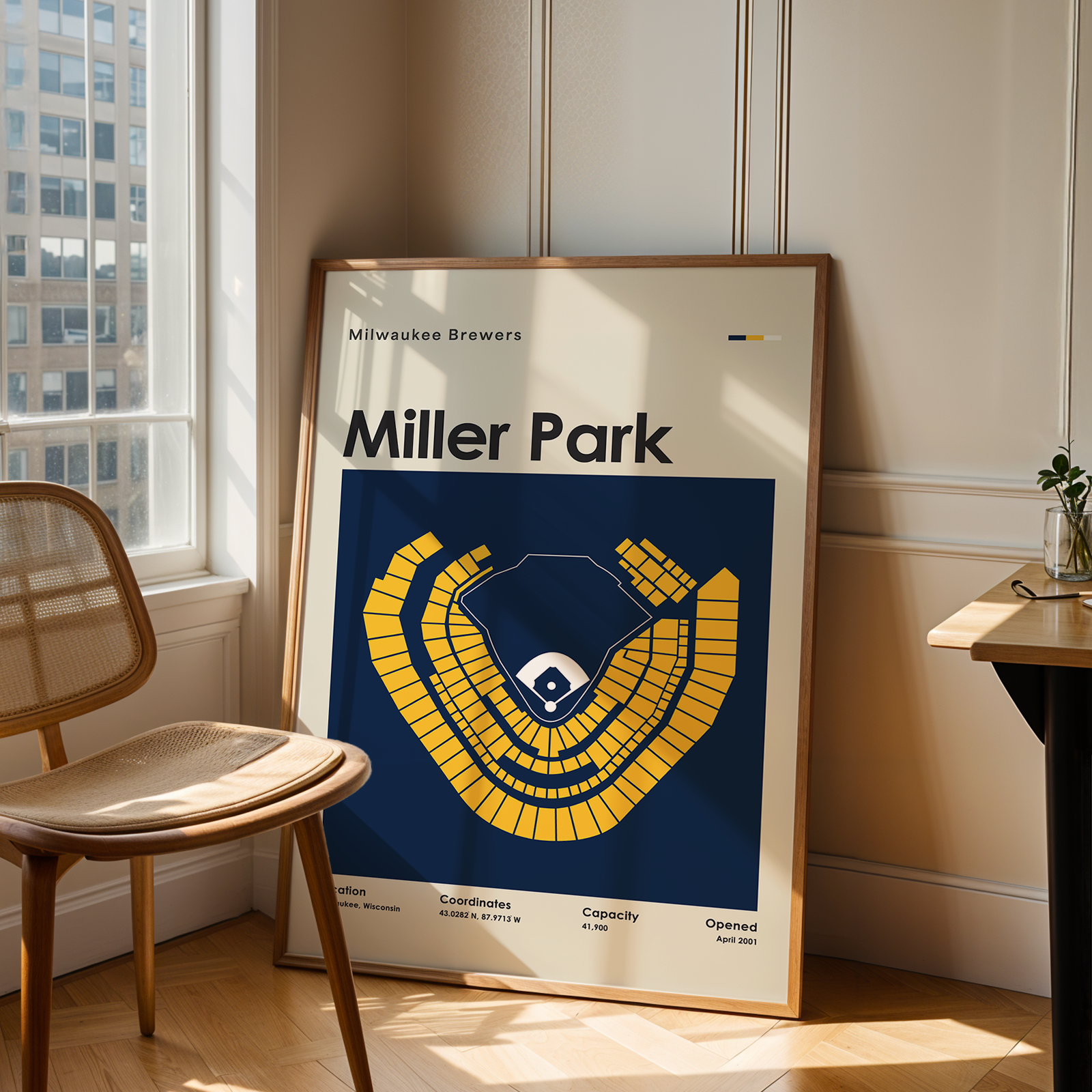 Framed poster of Miller Park in a room with a chair and table.