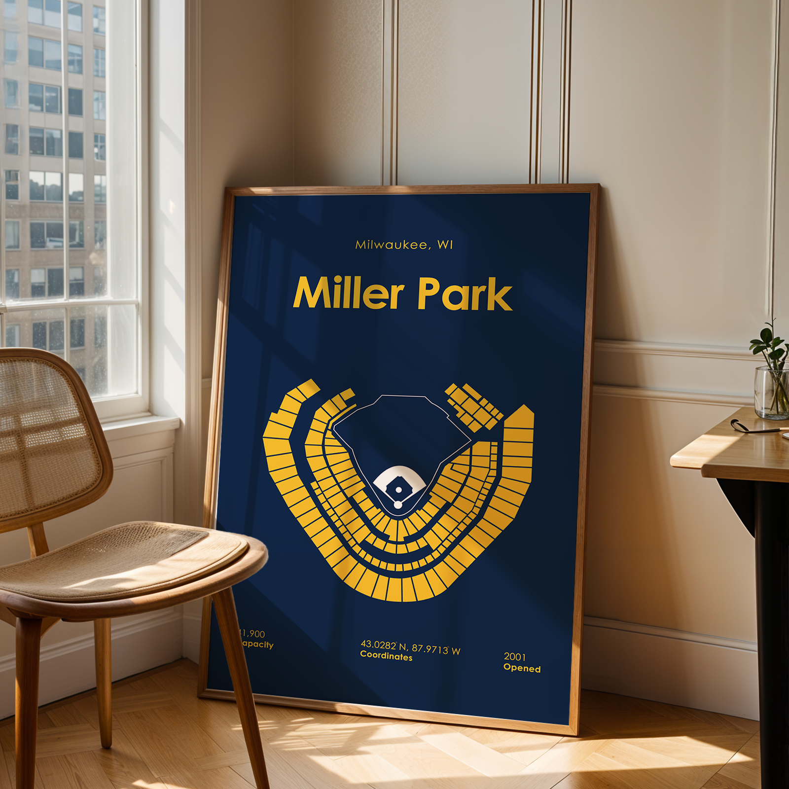 Framed poster of Miller Park in a room with a chair and table.