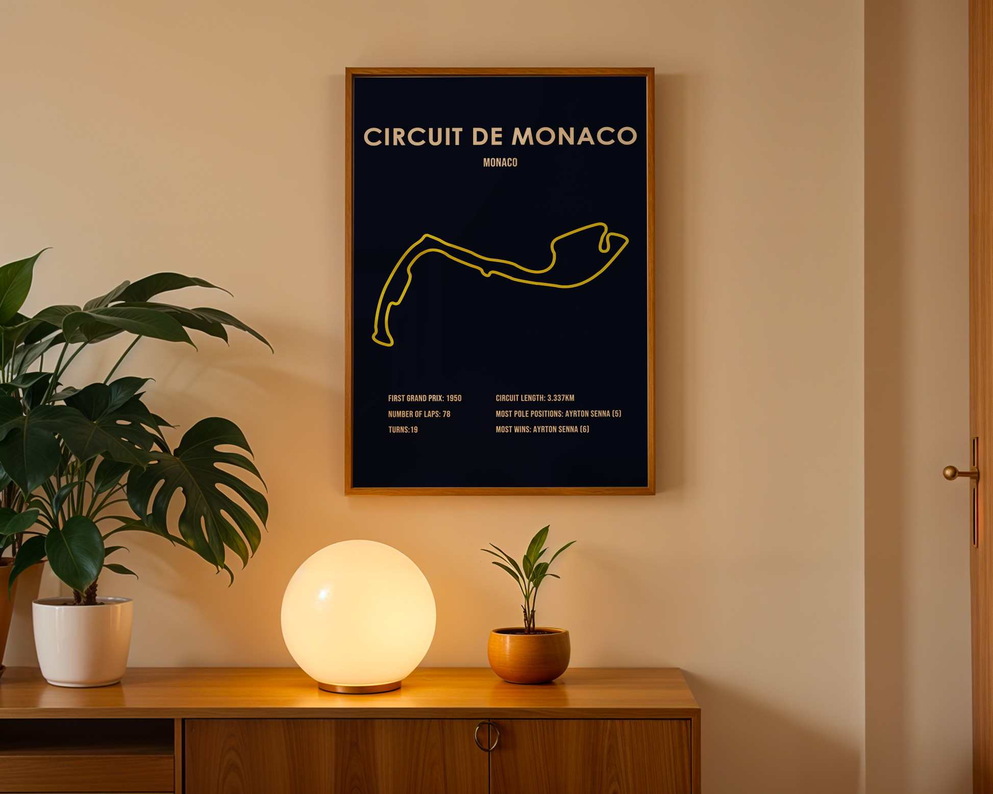 Framed poster of Circuit de Monaco on a wall with a plant and lamp below.