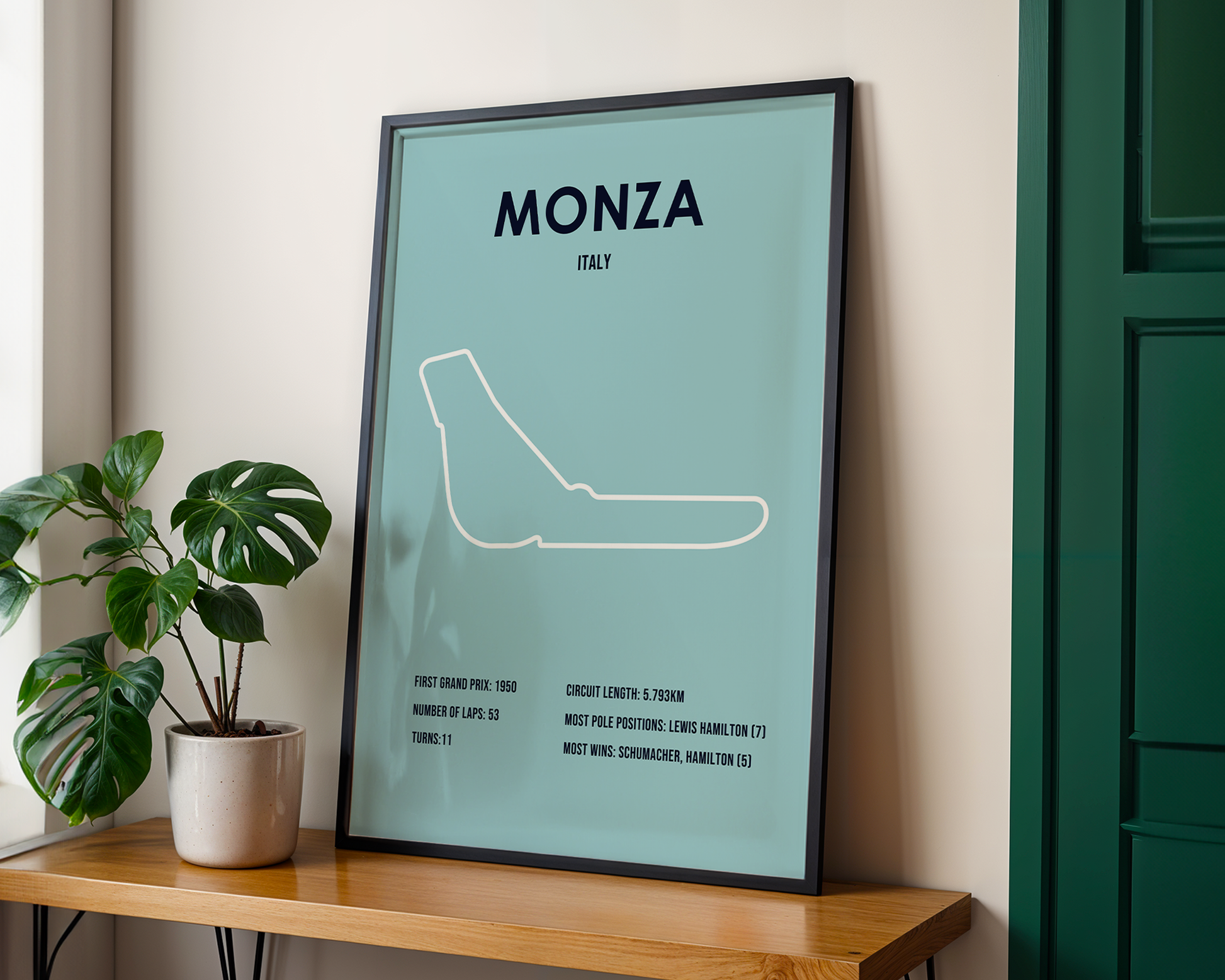 Framed poster of Monza circuit layout on a wall with a plant and wooden shelf.
