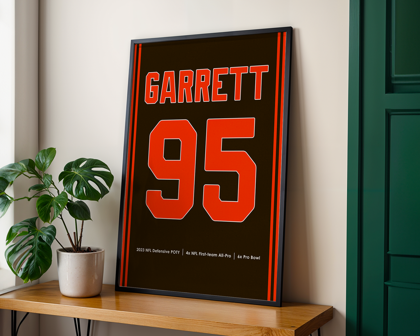 Framed poster with 'Garrett 95' on a wooden shelf next to a plant