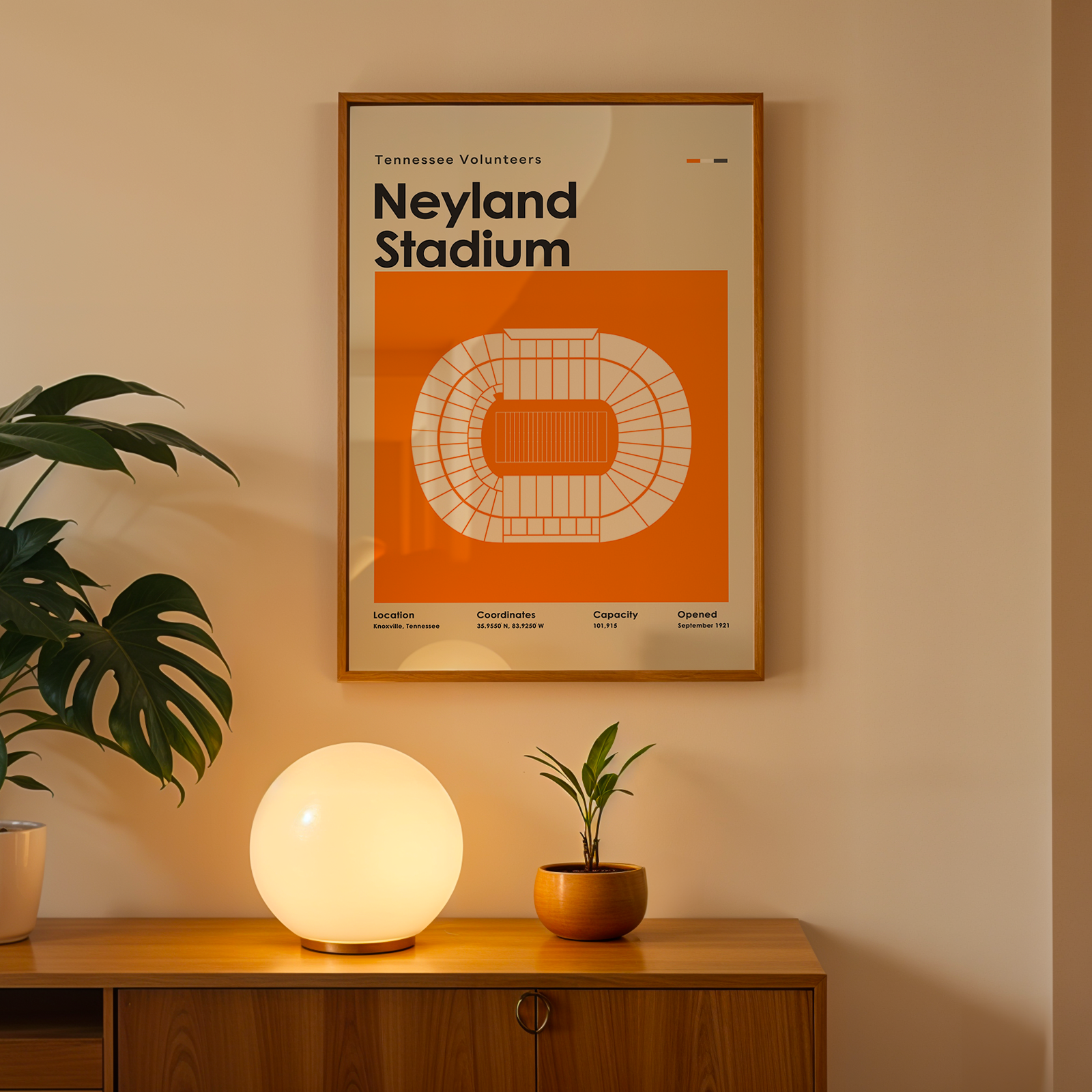 A framed poster of Neyland Stadium from the Tennessee Volunteers hanging on a beige wall above a wooden console table. The poster features an orange background with a white track-and-field graphic and black text.