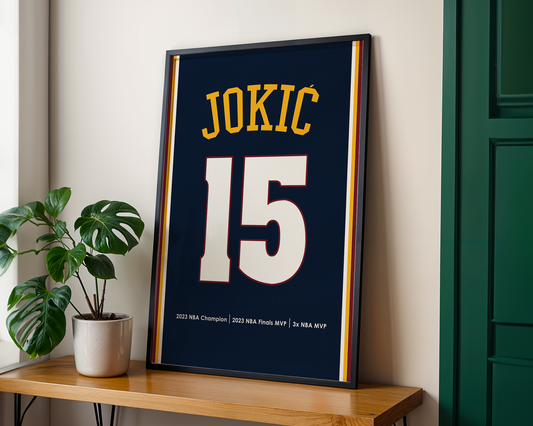 Framed sports jersey with 'JOKIC 15' on a wooden shelf with a plant.