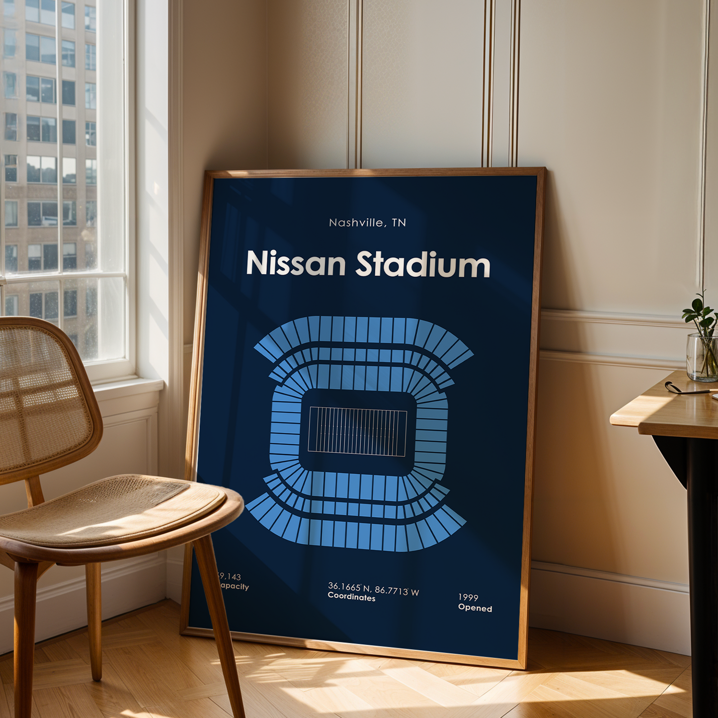 Framed poster of Nissan Stadium in Nashville, TN, leaning against a wall next to a chair and table.