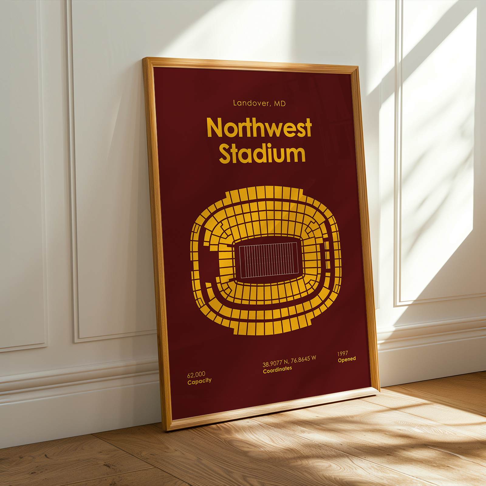 Framed poster of Northwest Stadium with a red background and yellow design, placed on a wooden floor.