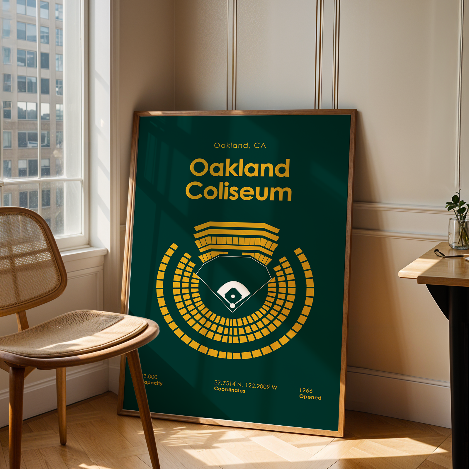 Framed poster of Oakland Coliseum in a room with a chair and table.