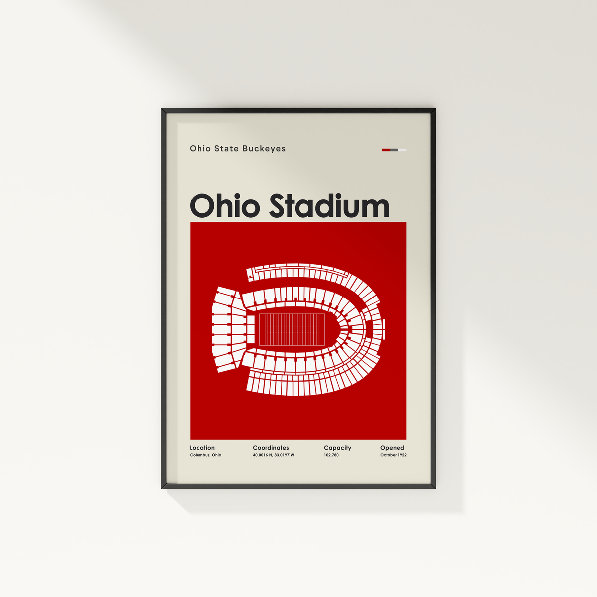 A framed Ohio State Buckeyes Ohio Stadium poster on a light gray wall. The poster features a bold red background with a white stadium layout and black text, enclosed in a thin black frame.