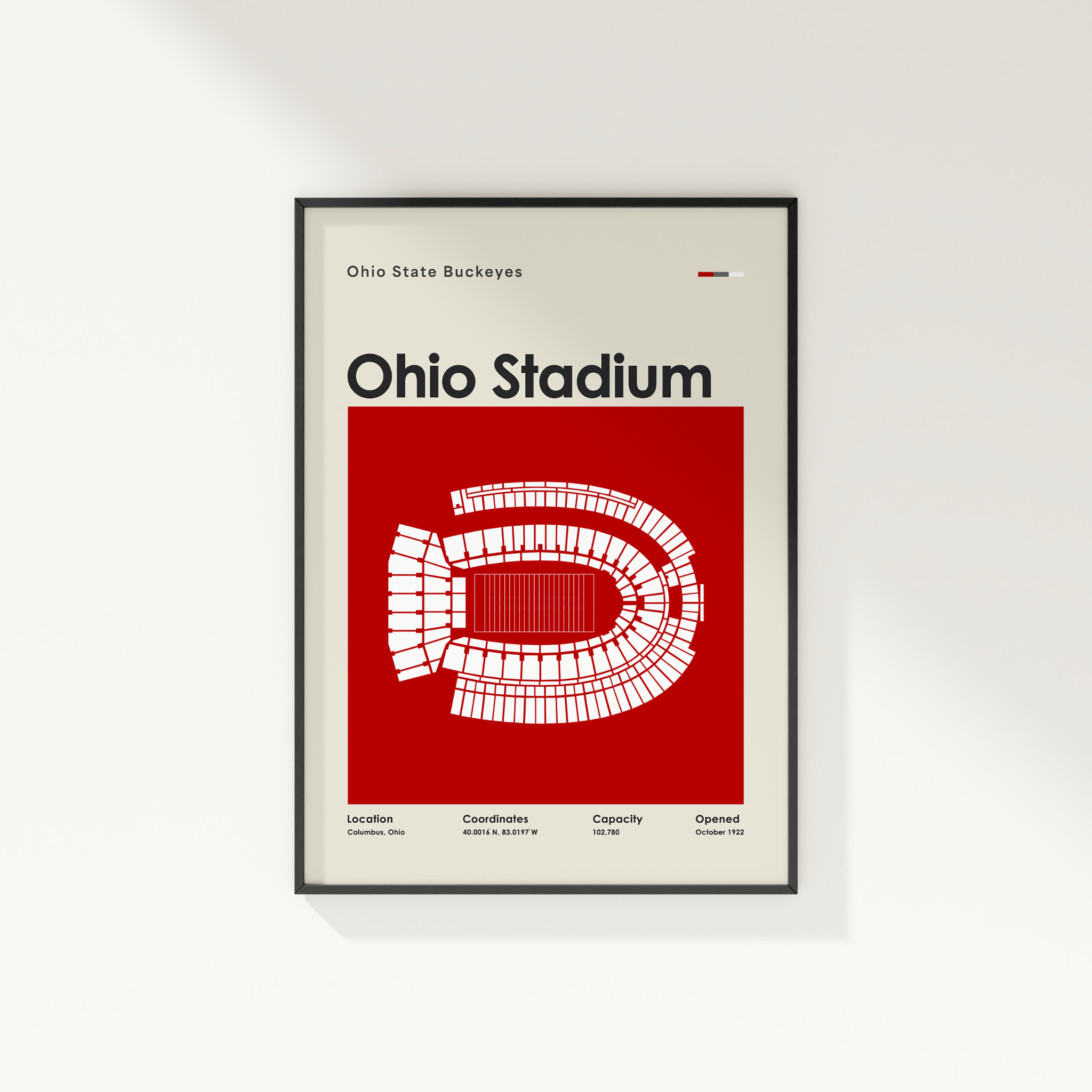 A framed Ohio State Buckeyes Ohio Stadium poster on a light gray wall. The poster features a bold red background with a white stadium layout and black text, enclosed in a thin black frame.