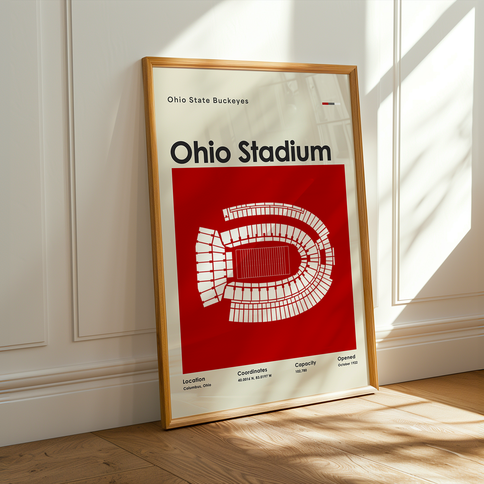 A framed Ohio State Buckeyes Ohio Stadium poster leaning against a white paneled wall on a light wood floor, with warm sunlight streaming across the scene.