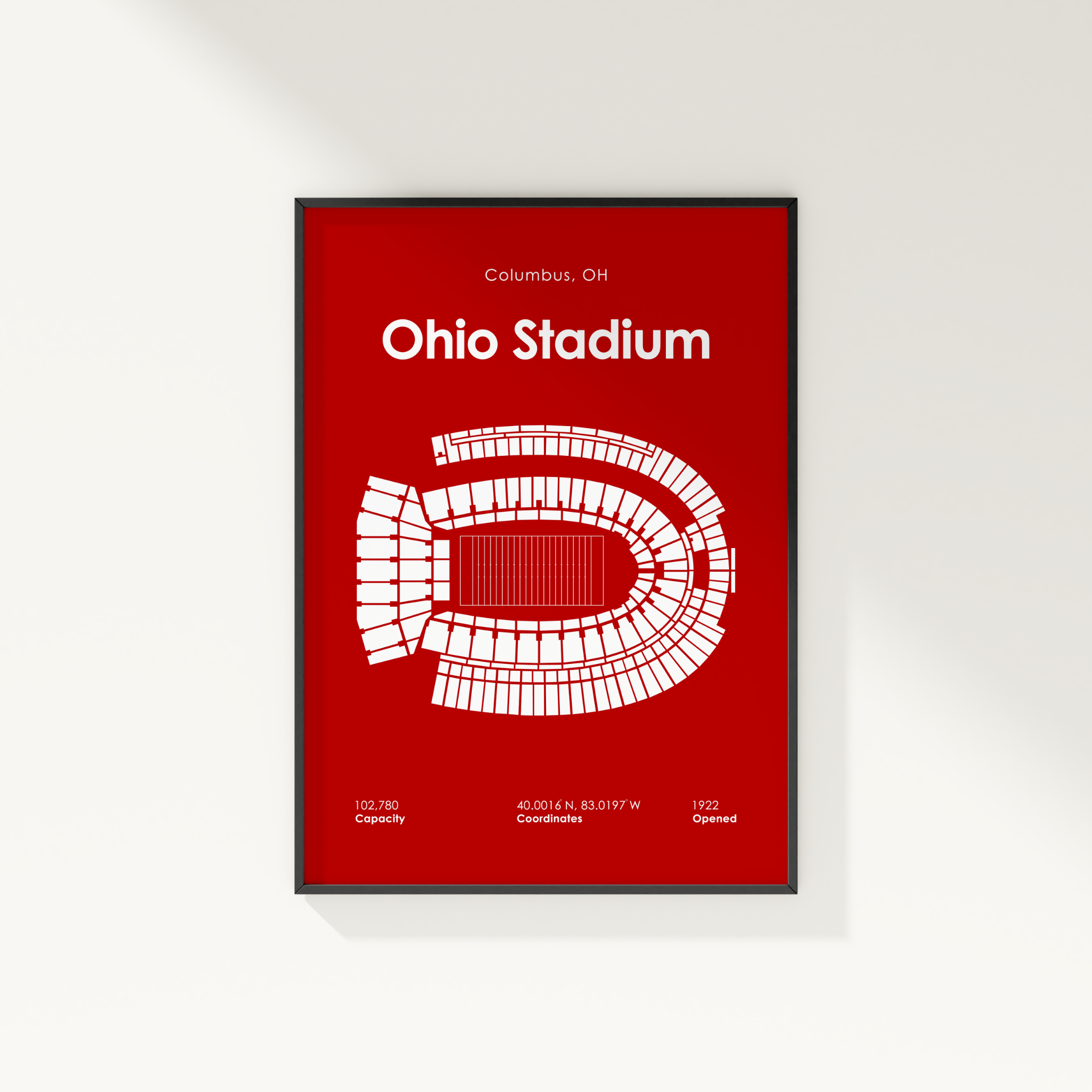 A framed vertical poster featuring a white stadium seating diagram and text reading 'Ohio Stadium' and 'Columbus, OH' on a solid red background, mounted on a light wall.