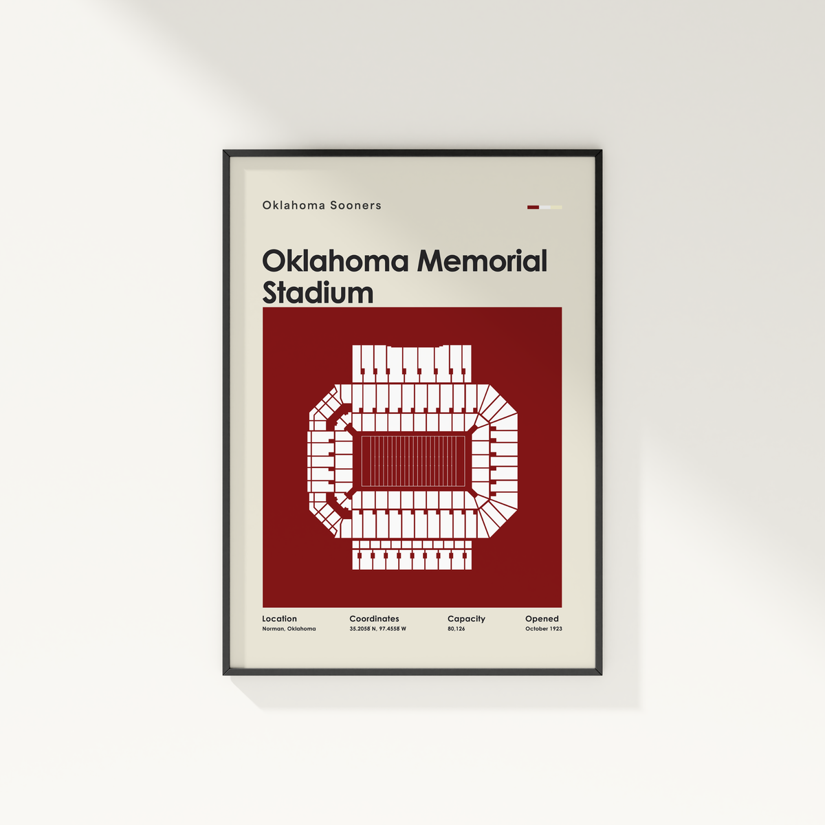 A framed Oklahoma Sooners Oklahoma Memorial Stadium poster hanging on a light gray wall. The poster features a cream background with a large dark red block, white stadium outline, and black text.