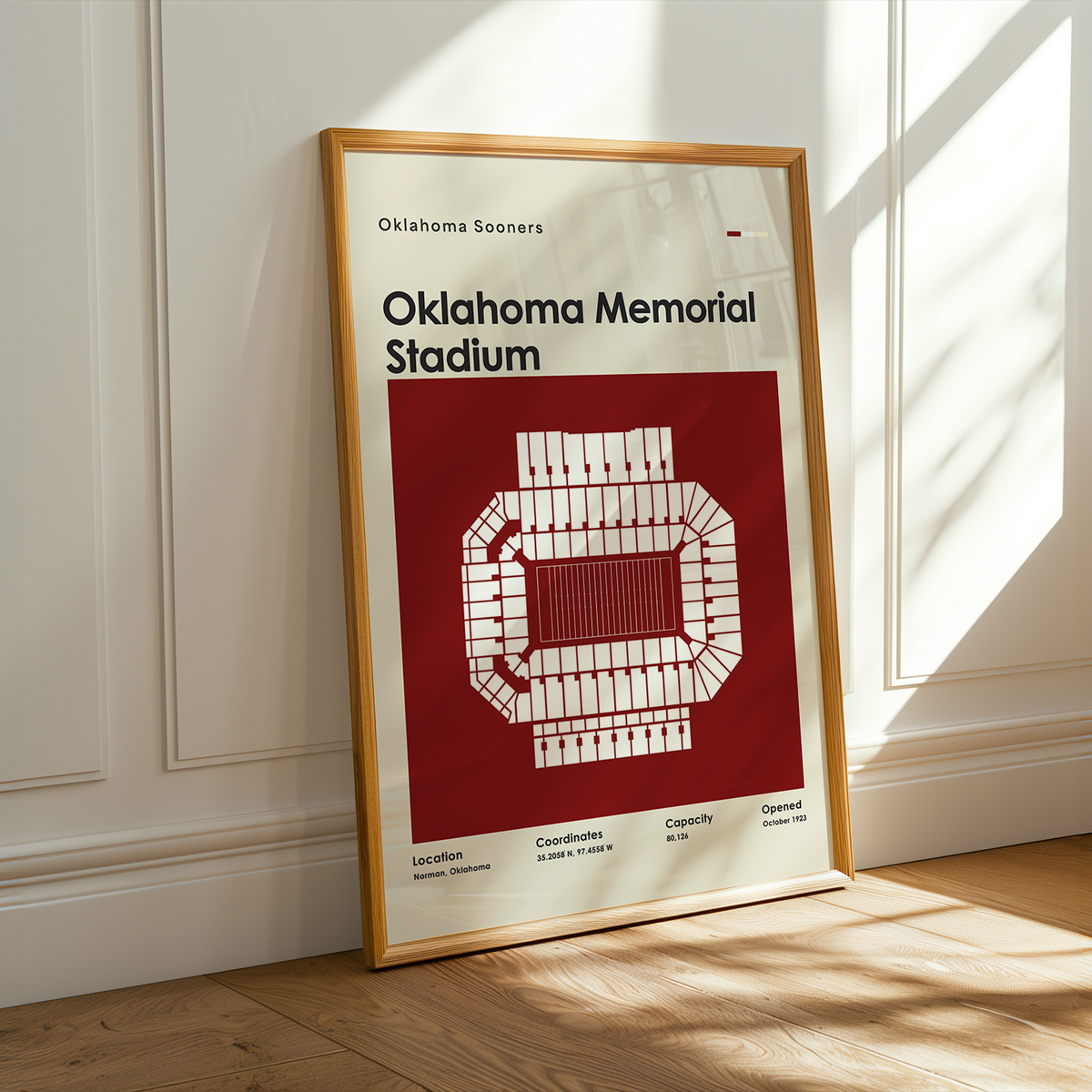 A framed Oklahoma Sooners Oklahoma Memorial Stadium poster leaning against a white paneled wall on a light wood floor, with warm sunlight streaming across the scene.